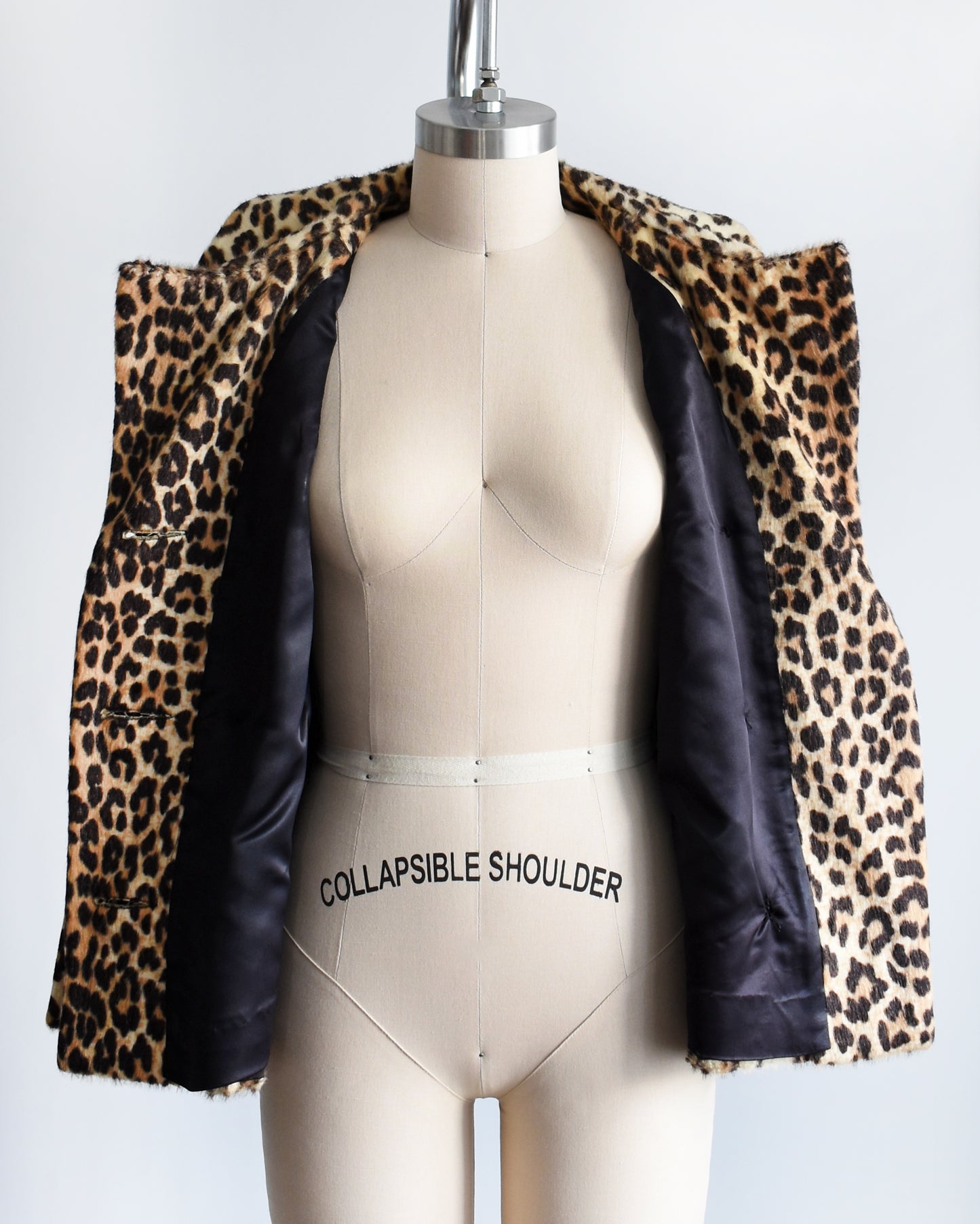 a vintage 1960s leopard print jacket on a mannequin. the jacket is opening showing the black lining against a white background