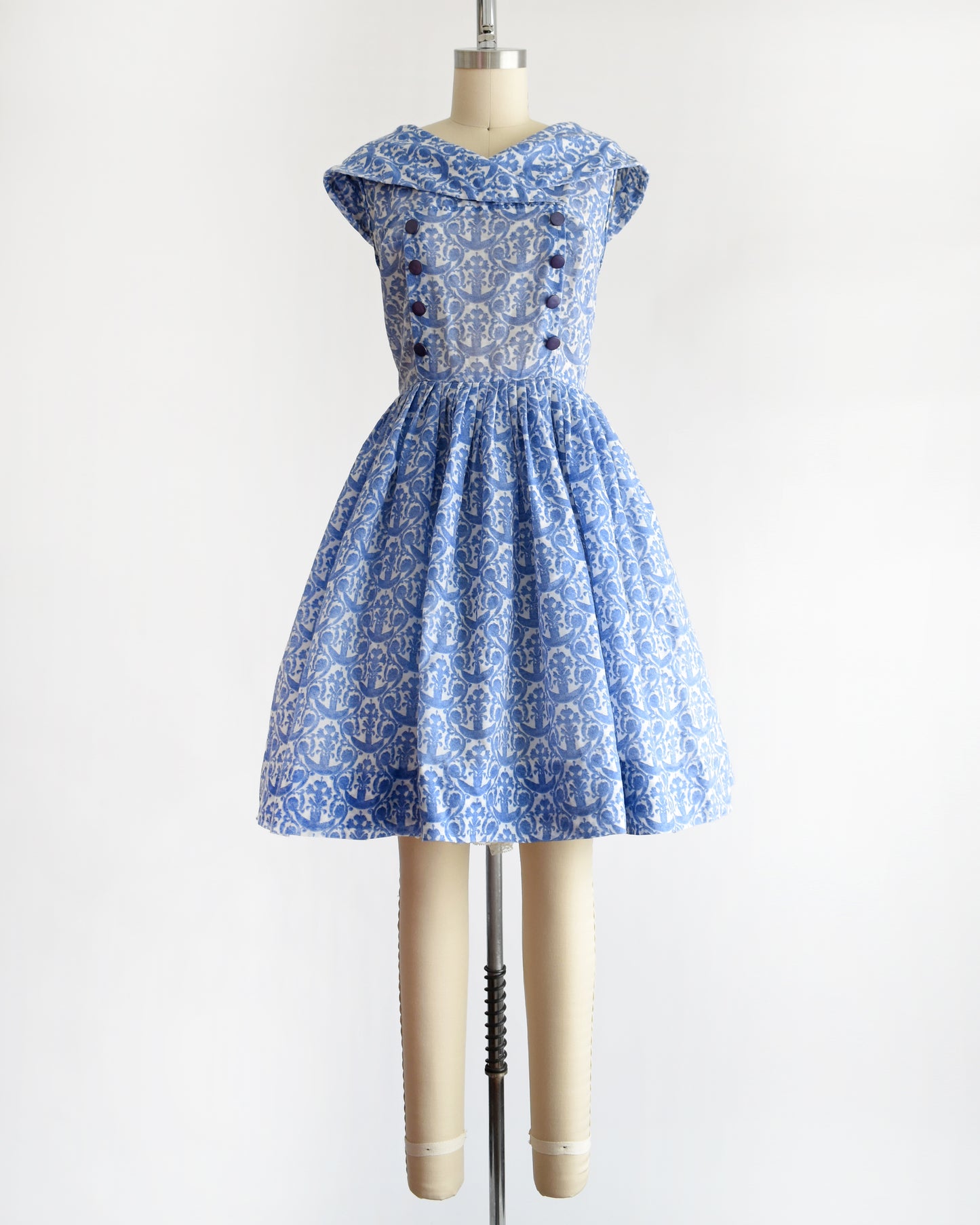a vintage 1960s blue and white patterned dress displayed on a beige dress form mannequin against a plain white background.