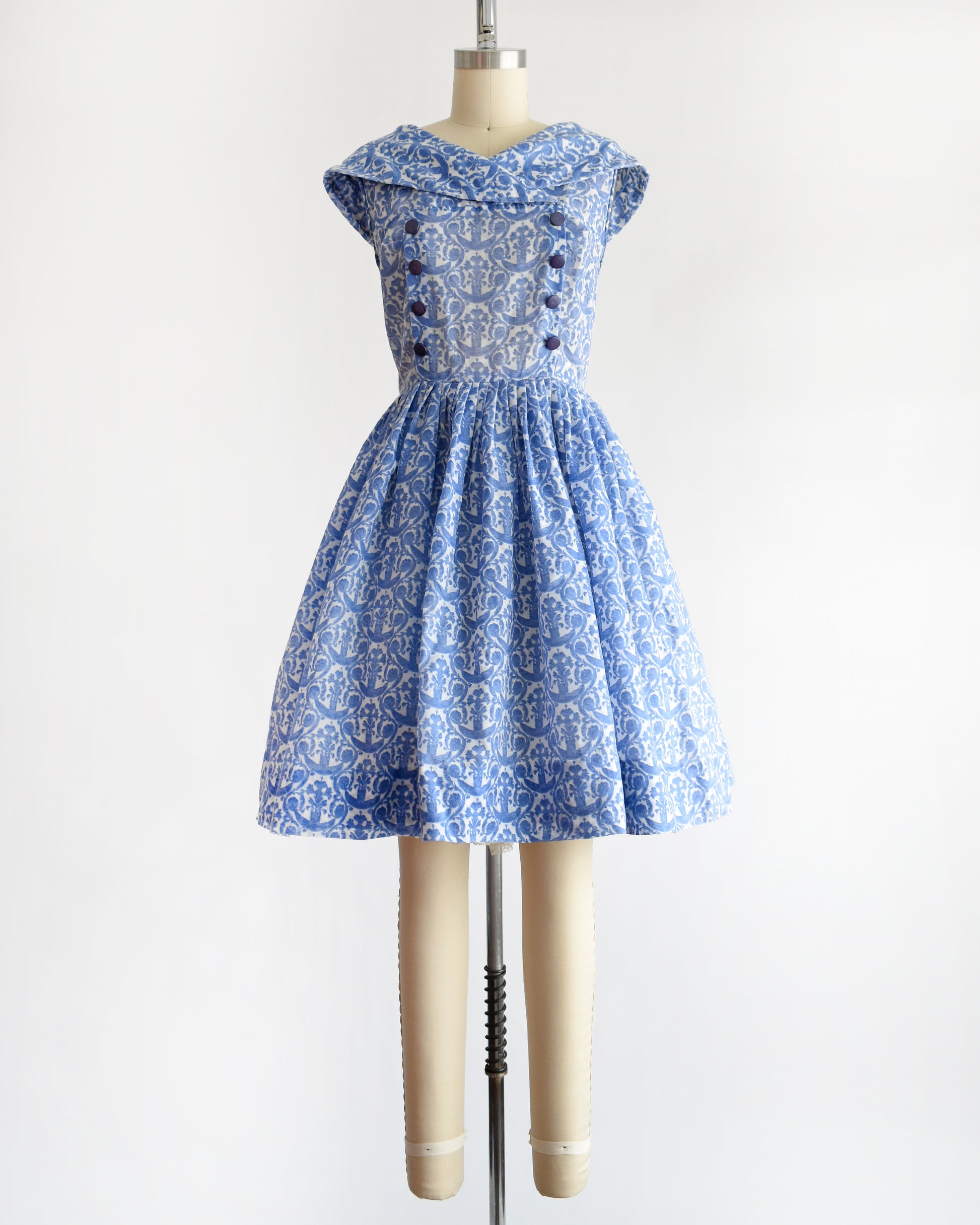 a vintage 1960s blue and white patterned dress displayed on a beige dress form mannequin against a plain white background.