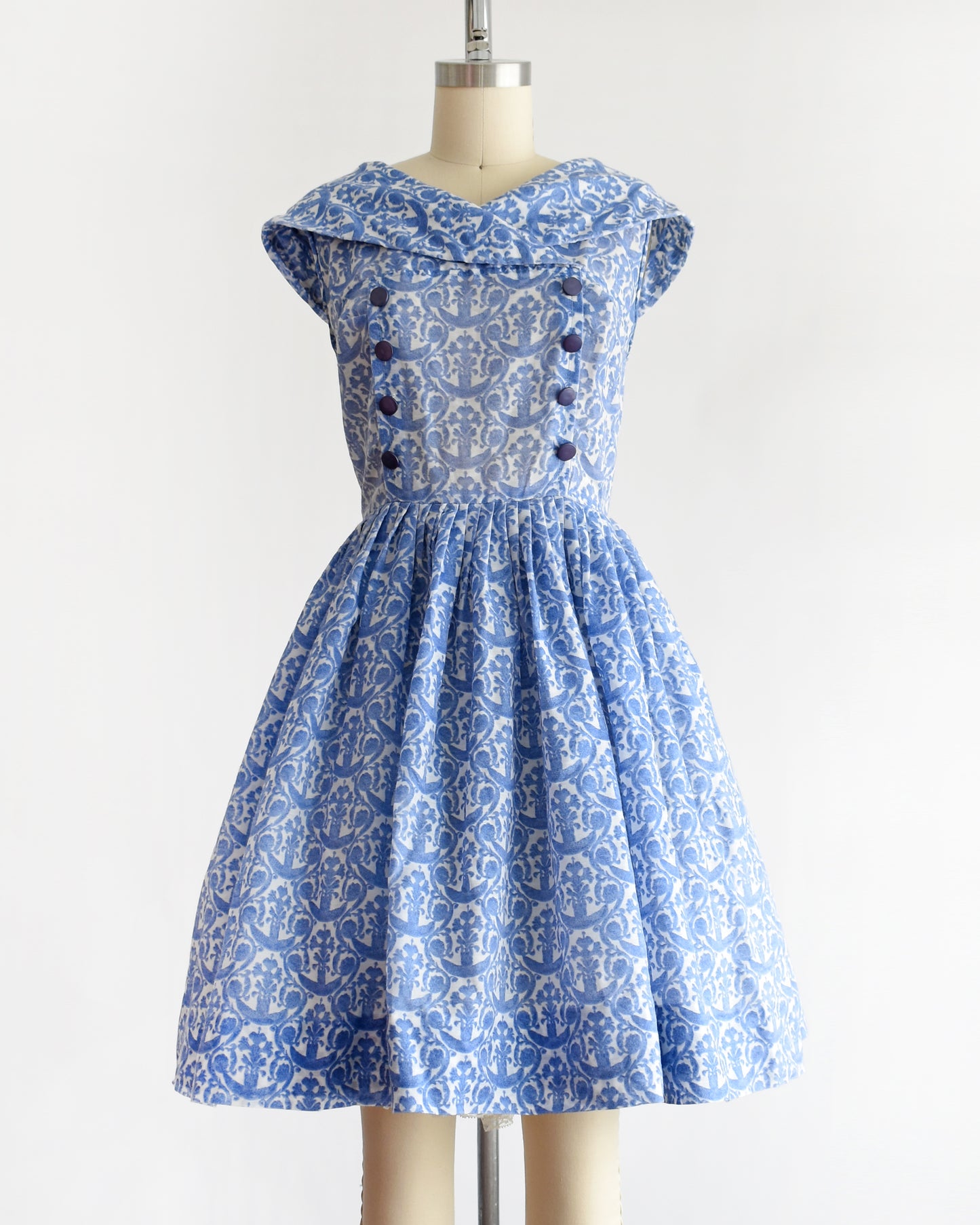 a vintage 1960s blue and white patterned dress displayed on a beige dress form mannequin against a plain white background.