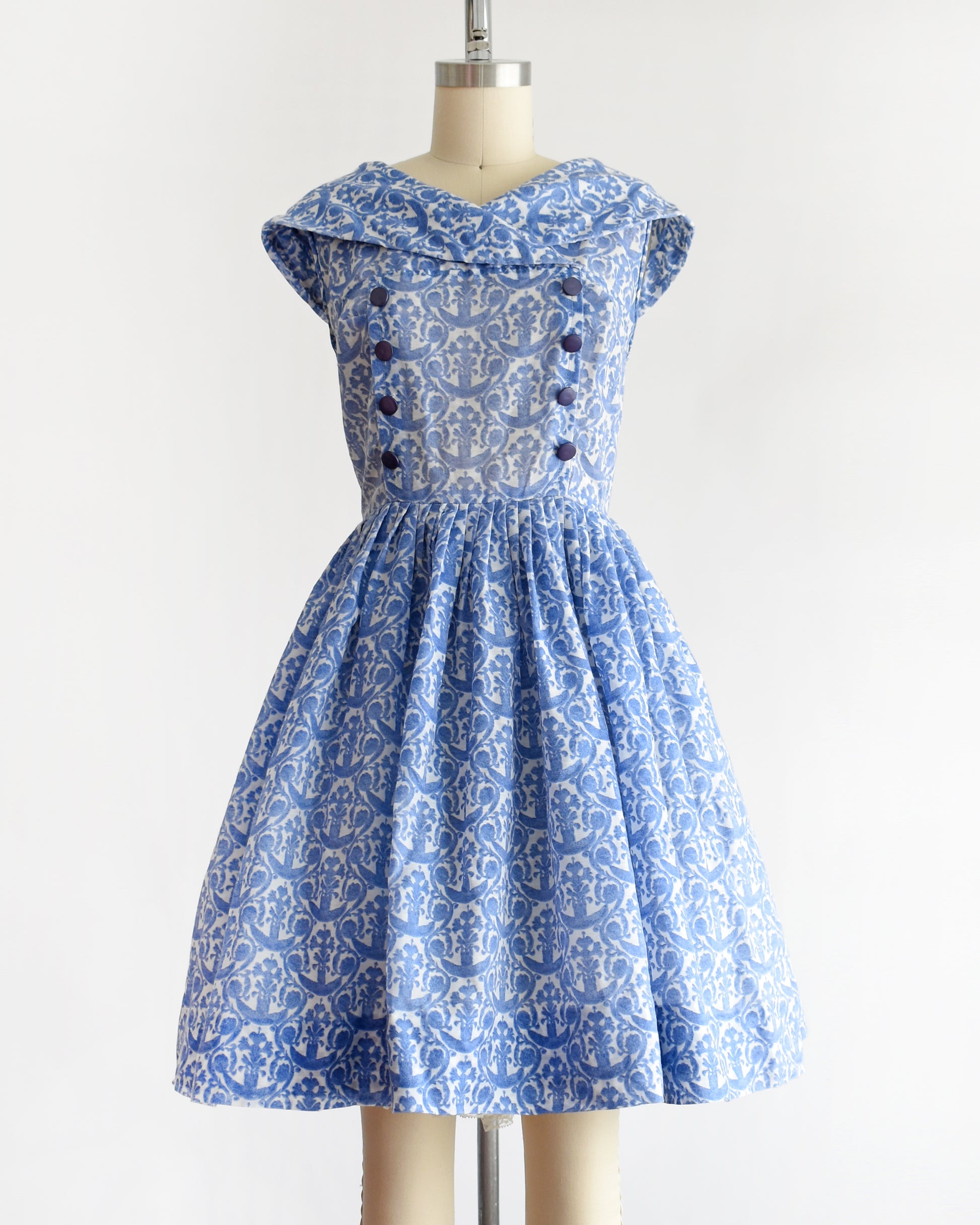 a vintage 1960s blue and white patterned dress displayed on a beige dress form mannequin against a plain white background.
