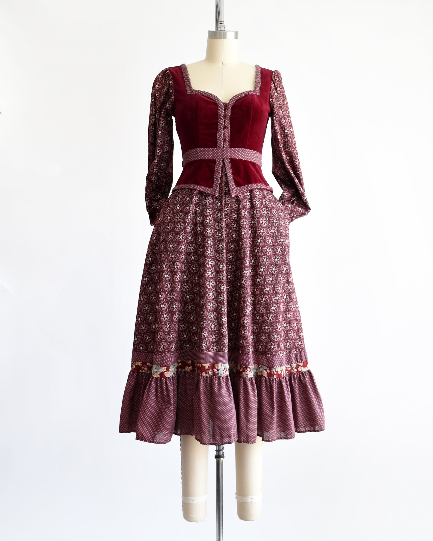 a vintage 1970s Gunne Sax dress that is burgundy and has a velvet bodice and floral skirt and long sleeves. The sleeves are in the pocket in this photo