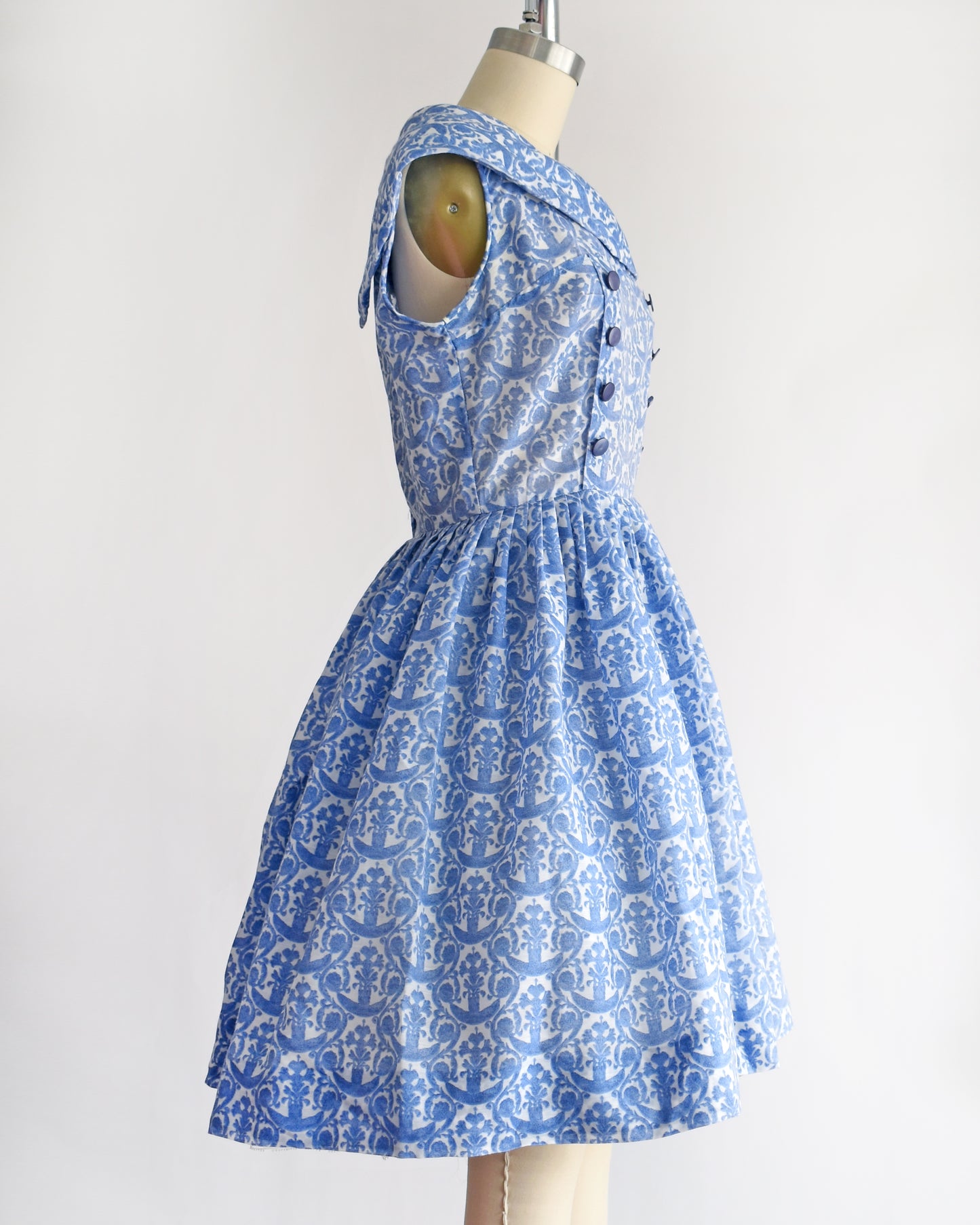 side view of a vintage 1960s blue and white patterned dress displayed on a beige dress form mannequin against a plain white background.