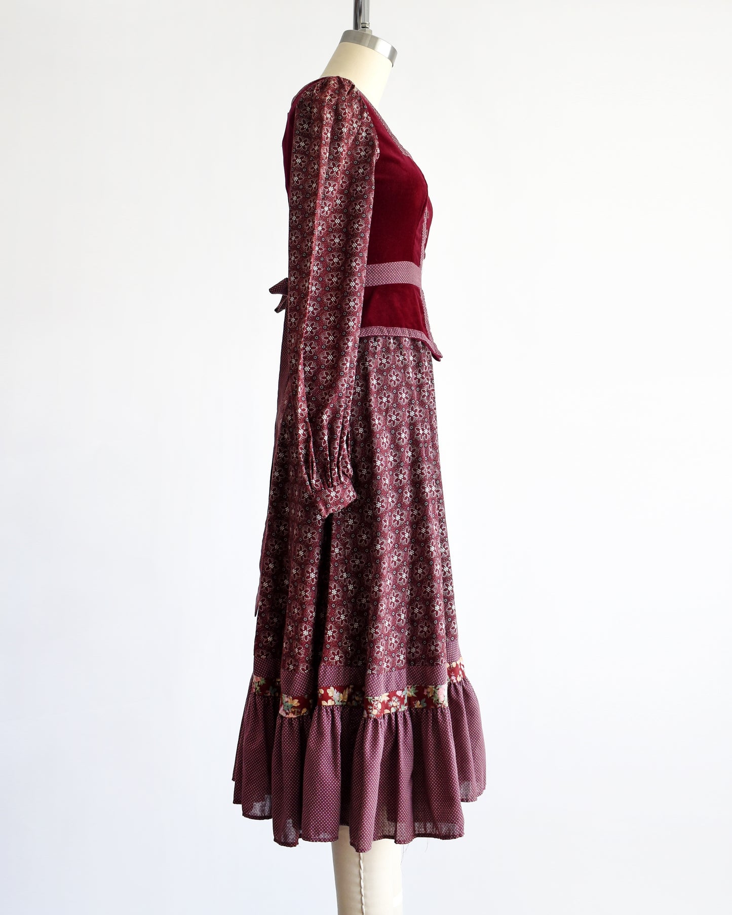 side view of a vintage 1970s Gunne Sax dress that is burgundy and has a velvet bodice and floral skirt and long sleeves