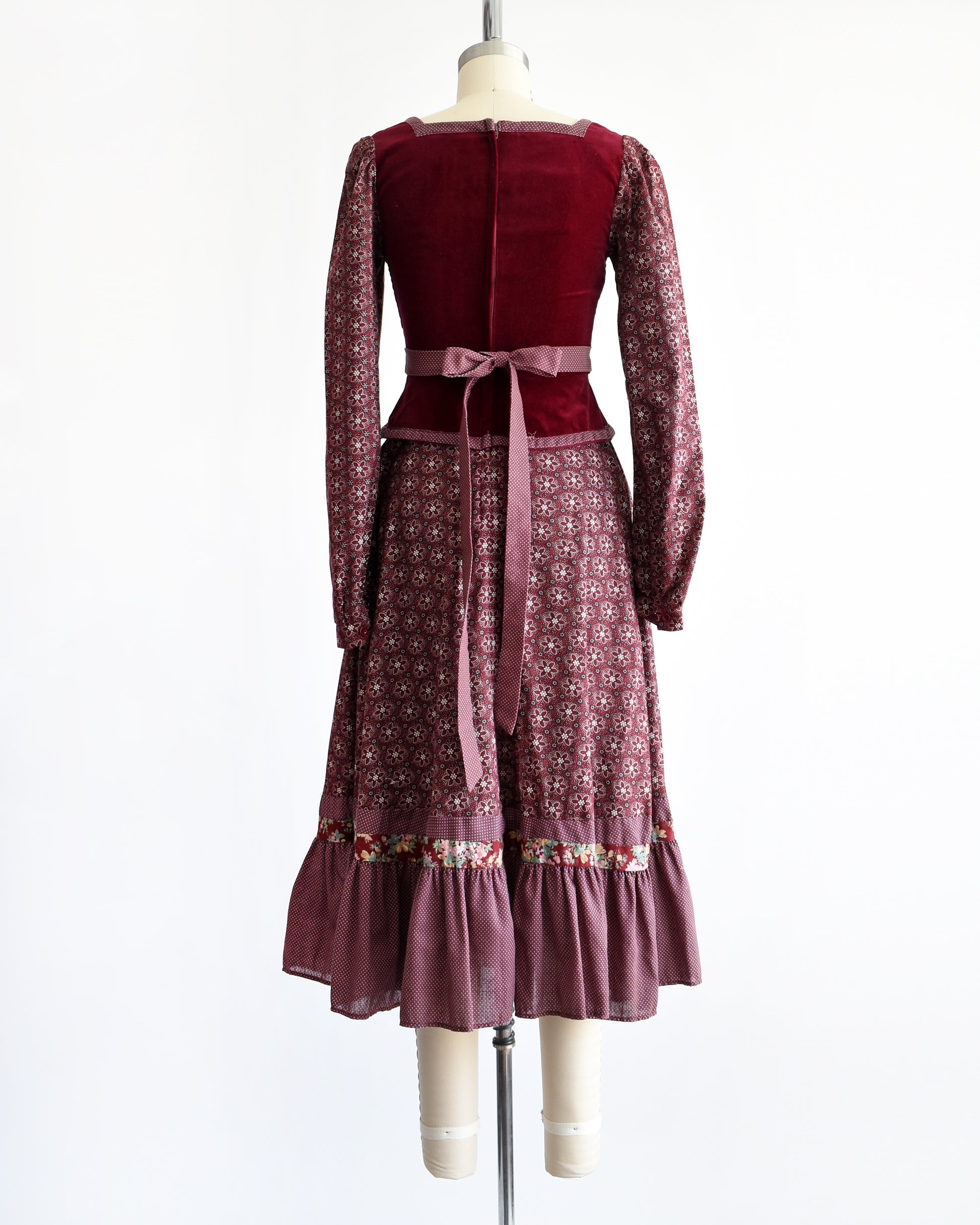 back view of a vintage 1970s Gunne Sax dress that is burgundy and has a velvet bodice and floral skirt and long sleeves