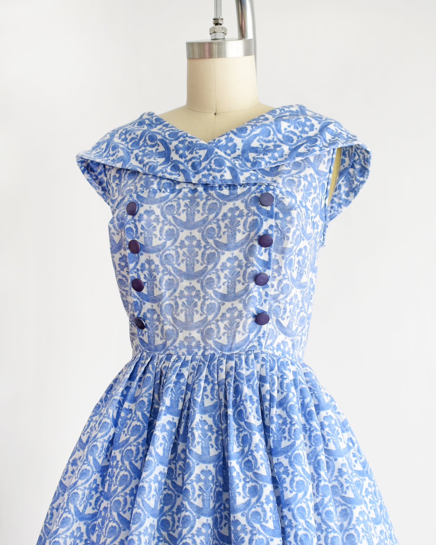 side front view of a vintage 1960s blue and white patterned dress displayed on a beige dress form mannequin against a plain white background.