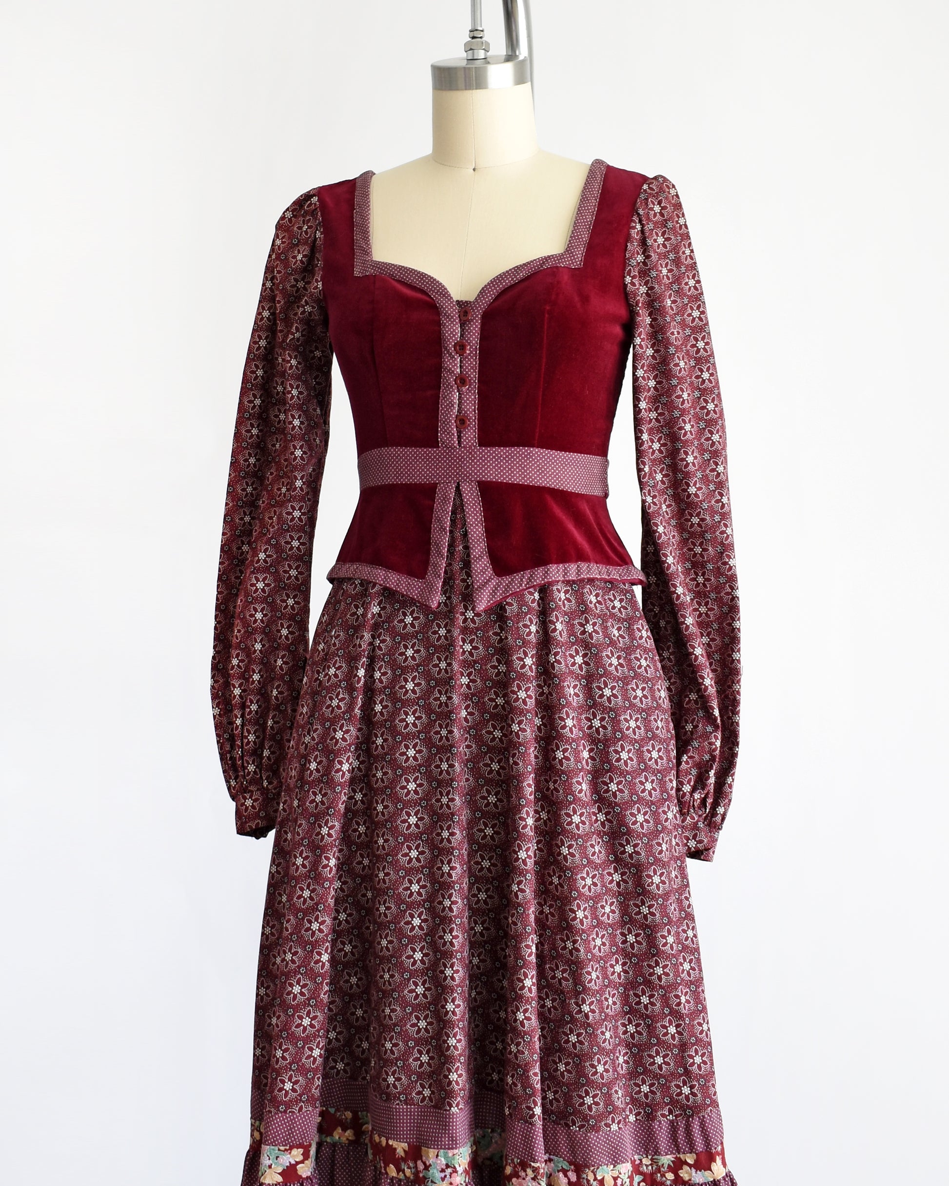 side front view of a vintage 1970s Gunne Sax dress that is burgundy and has a velvet bodice and floral skirt and long sleeves