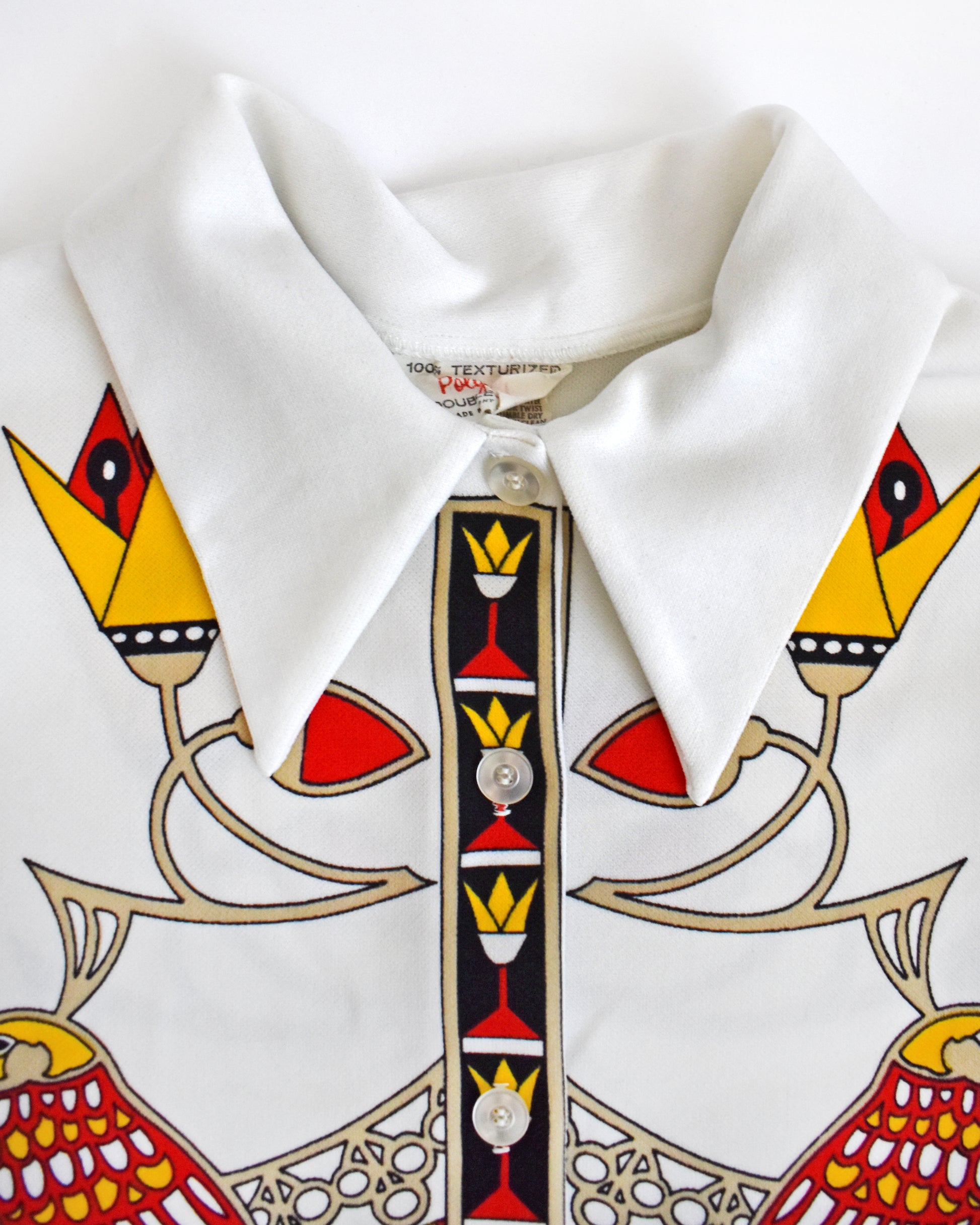 close up of the collar on  a vintage 1970s white sleeveless top with a colorful abstract bird design on a white background
