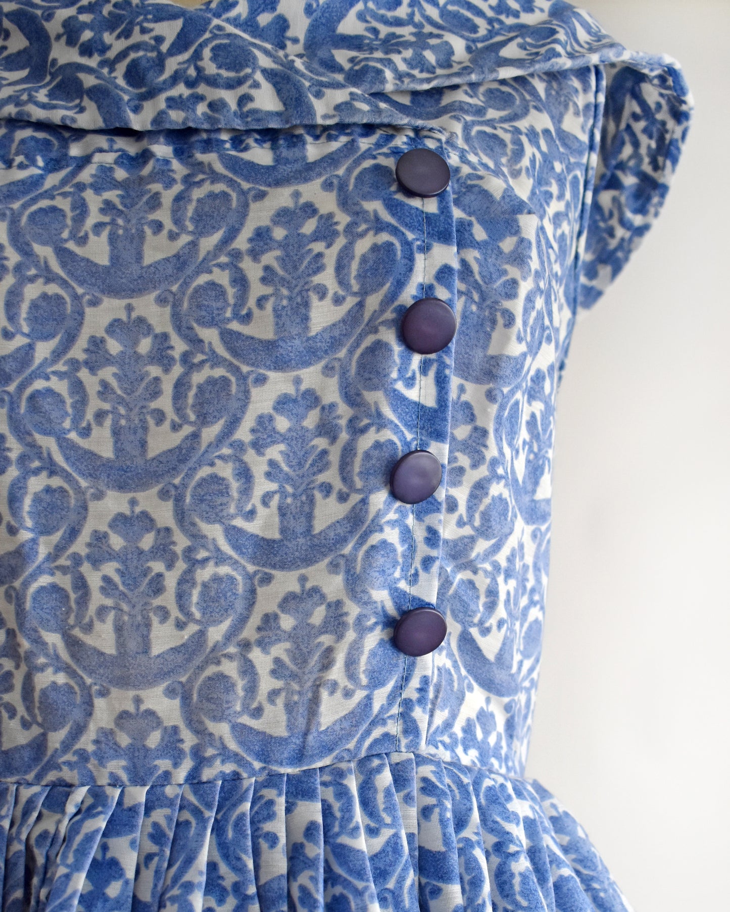 Close-up of a blue and white damask-patterned dress with dark blue buttons on the front.