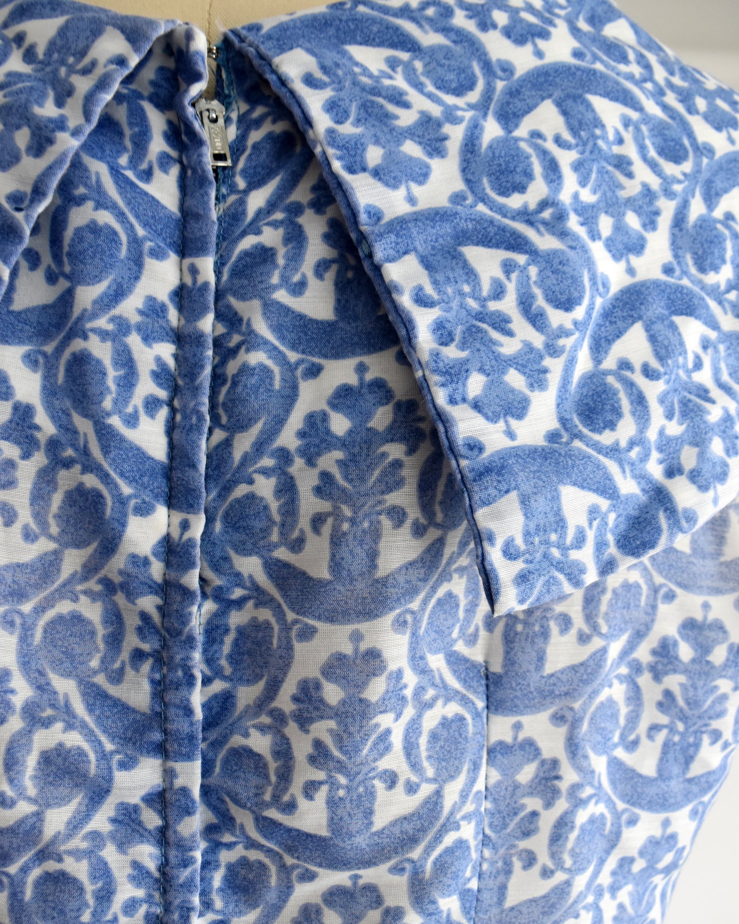 close up of the back of the collar on a vintage 1960s blue and white patterned dress displayed on a beige dress form mannequin against a plain white background.