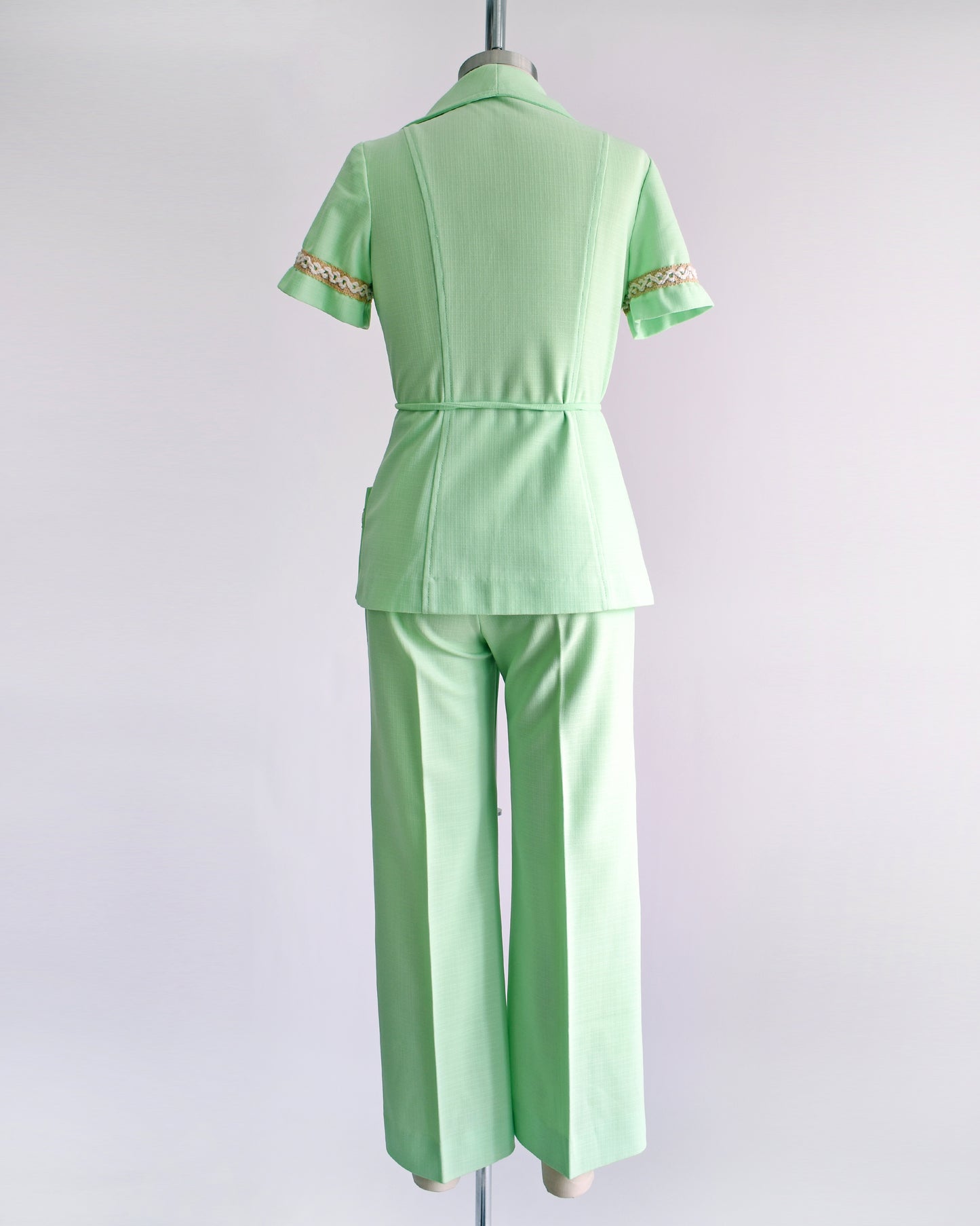 back view of a vintage 1970s mint green pantsuit that has a matching blazer, a tie belt, and wide leg pants