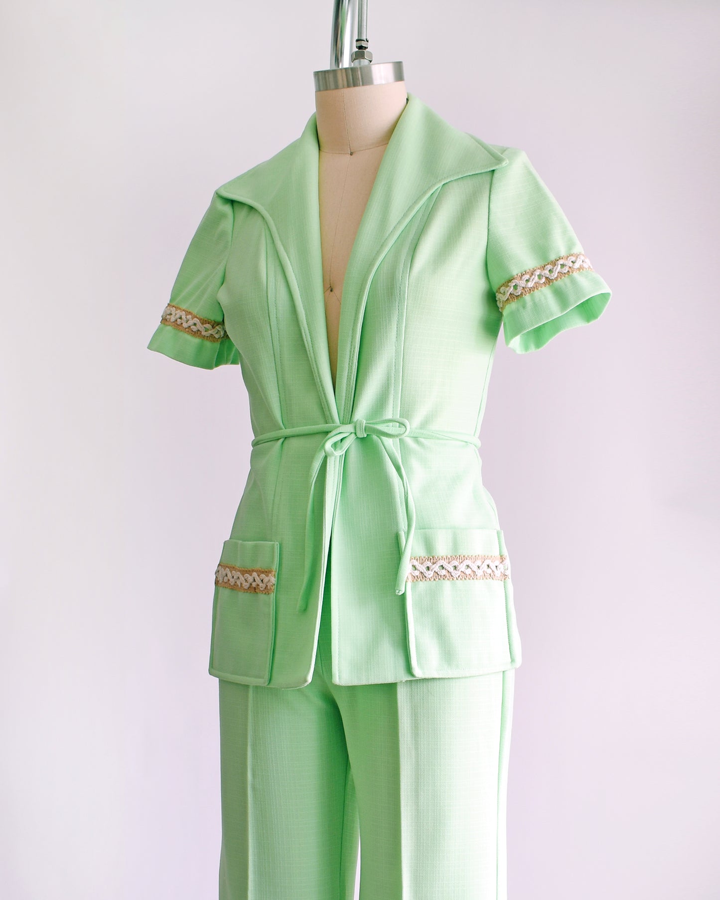 side front view of a vintage 1970s mint green pantsuit that has a matching blazer, a tie belt, and wide leg pants