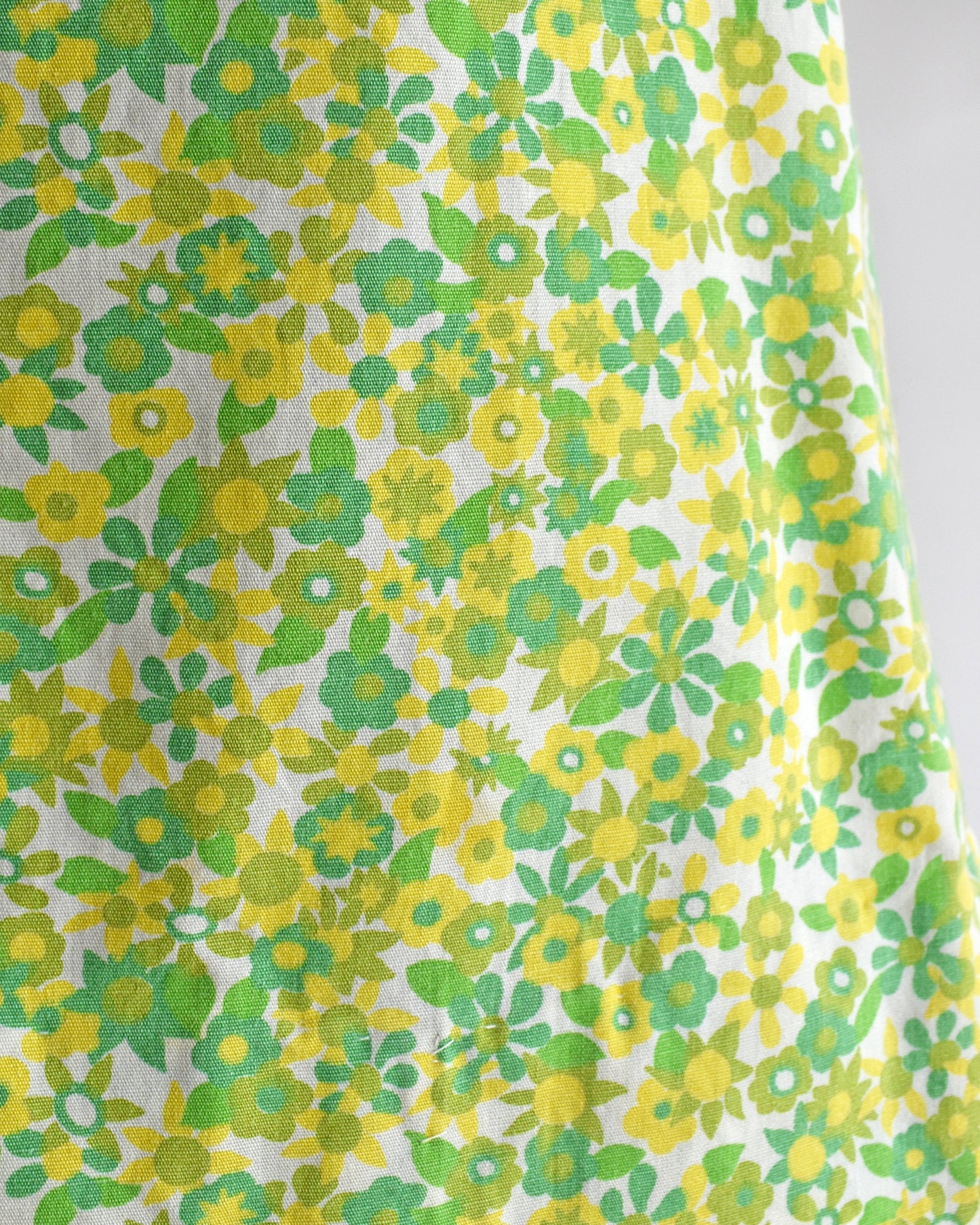 A close-up of a white fabric with a retro 1970s floral pattern featuring yellow and green flowers and leaves.