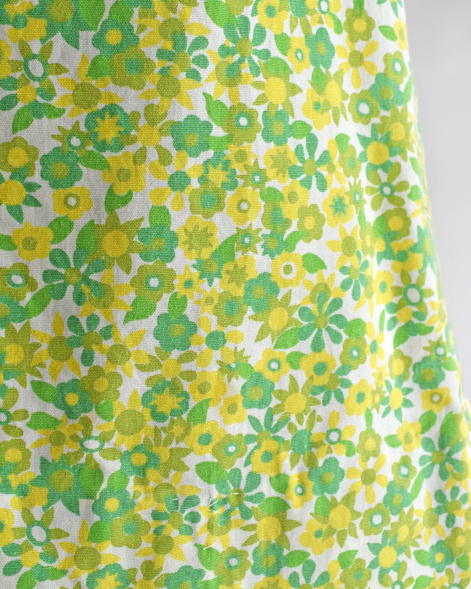 A close-up of a white fabric with a retro 1970s floral pattern featuring yellow and green flowers and leaves.