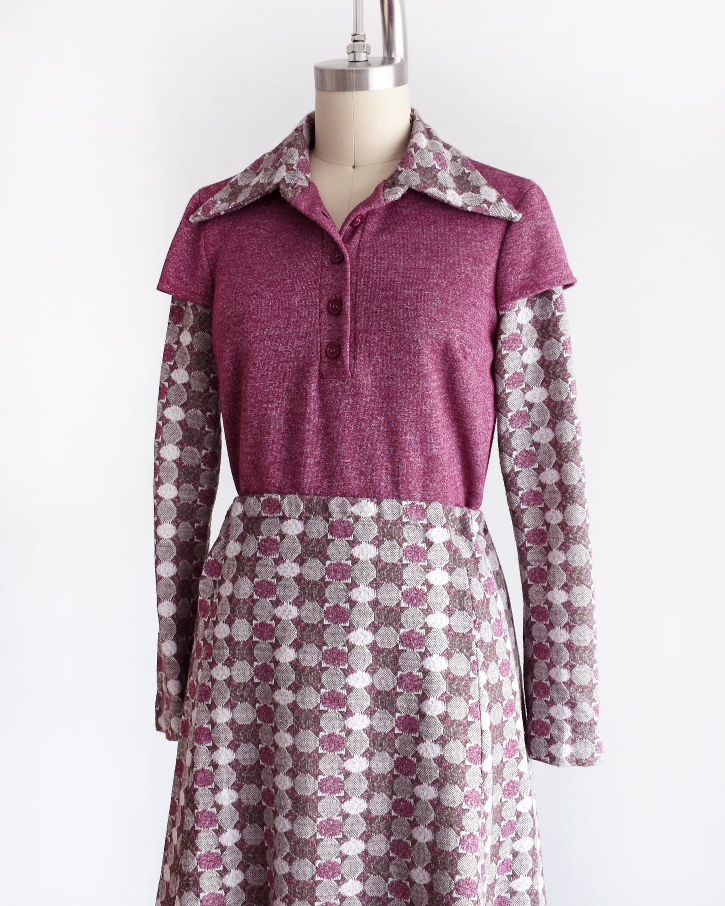 a vintage 1970s dress set that has a purple top and patterned skirt on a mannequin against a white background. the top has a few buttons unbuttoned at the collar.