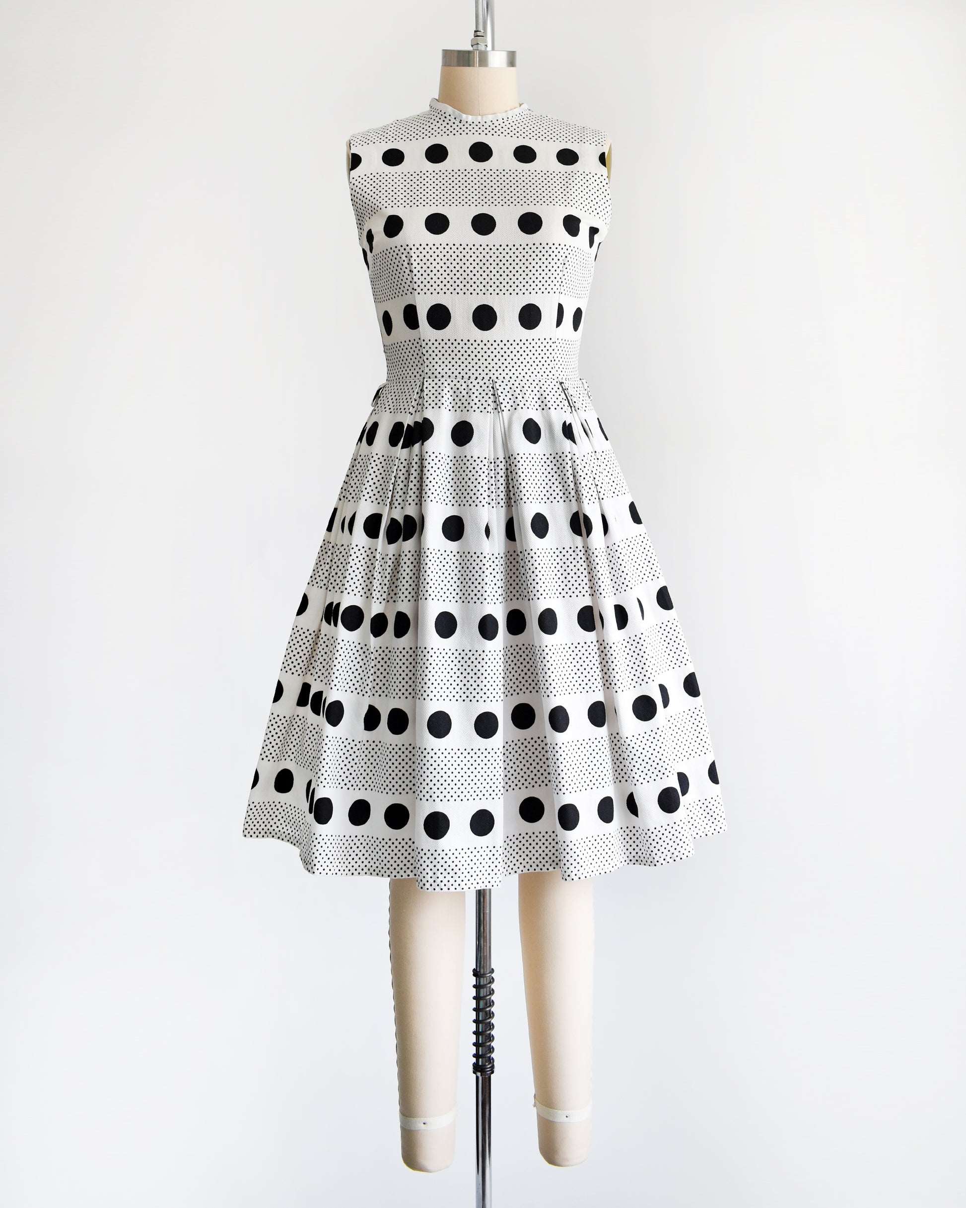 a vintage 1960s polka dot dress that is white cotton piqué with large and small black polka dots in a striped pattern on a dress form