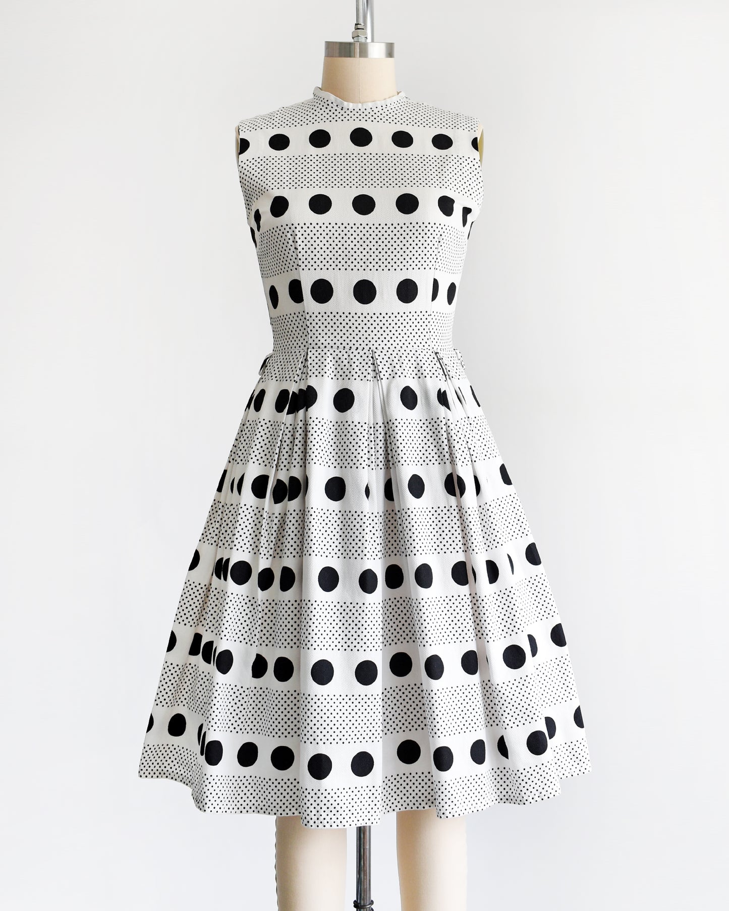 a vintage 1960s polka dot dress that is white cotton piqué with large and small black polka dots in a striped pattern on a dress form