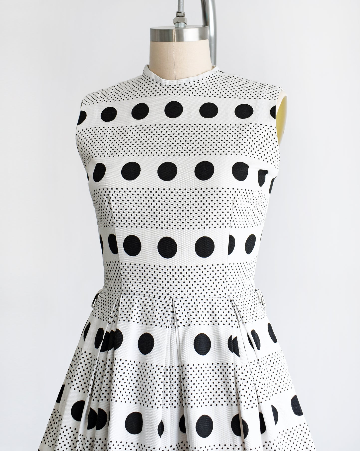 side front view of the bodice of a vintage 1960s polka dot dress that is white cotton piqué with large and small black polka dots in a striped pattern on a dress form