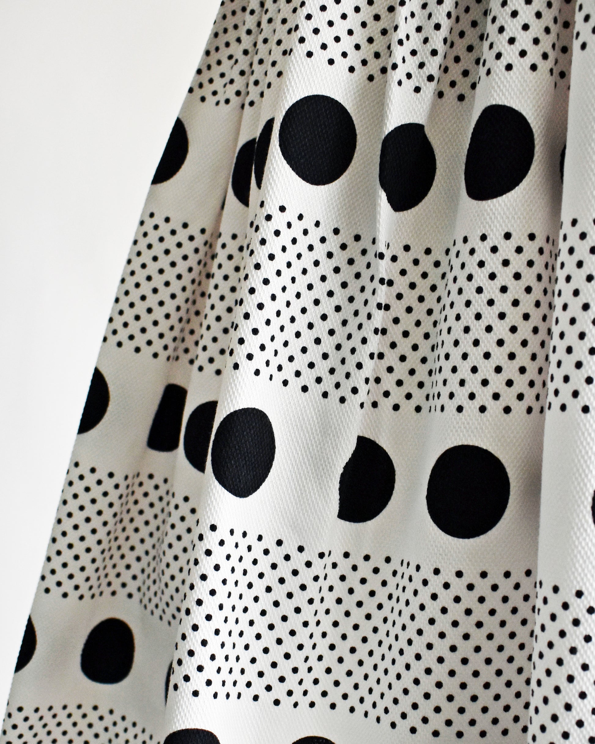 close up of the skirt of a vintage 1960s polka dot dress that is white cotton piqué with large and small black polka dots in a striped pattern on a dress form