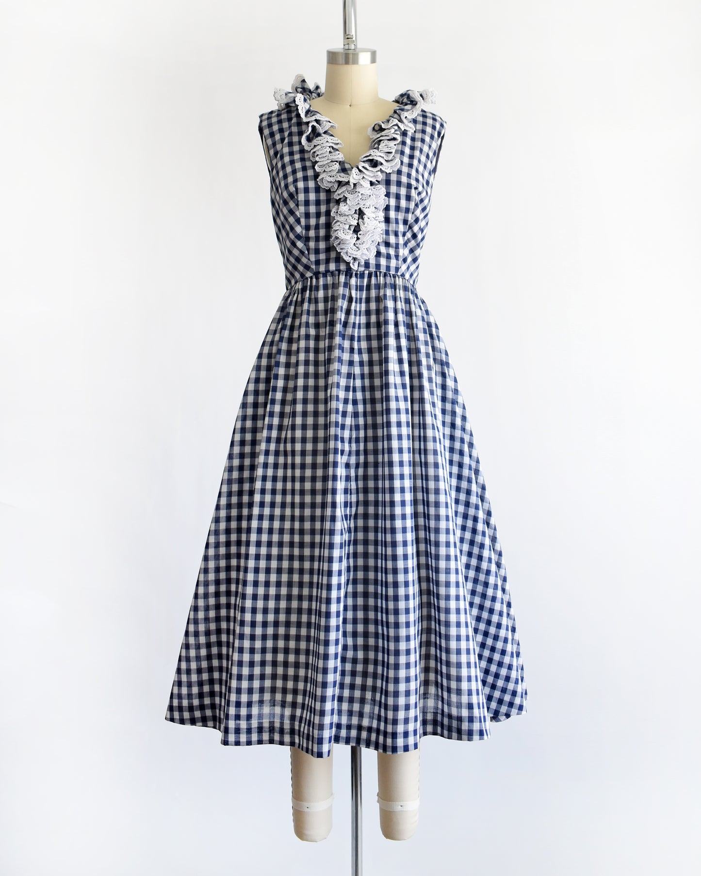 a vintage 1960s sleeveless blue and white gingham dress displayed on a cream dress form against a plain white background.