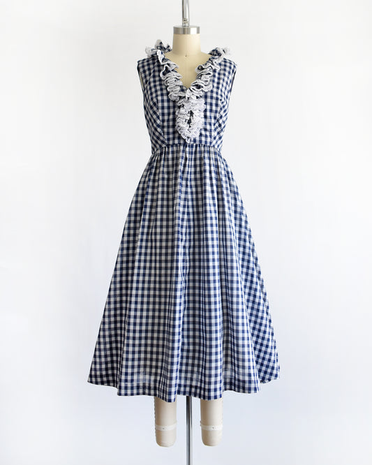 a vintage 1960s sleeveless blue and white gingham dress displayed on a cream dress form against a plain white background.