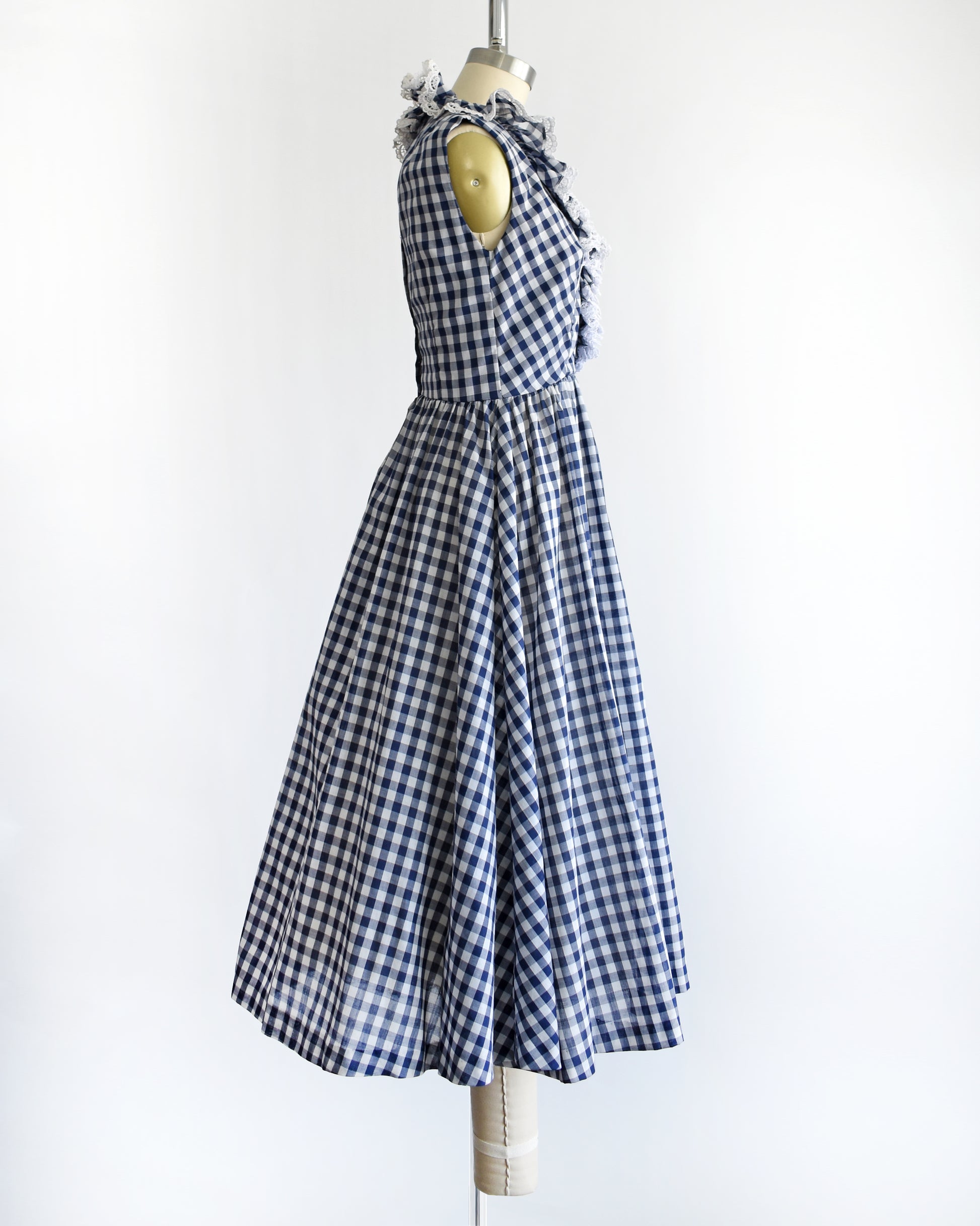 side view of a vintage 1960s sleeveless blue and white gingham dress displayed on a cream dress form against a plain white background.
