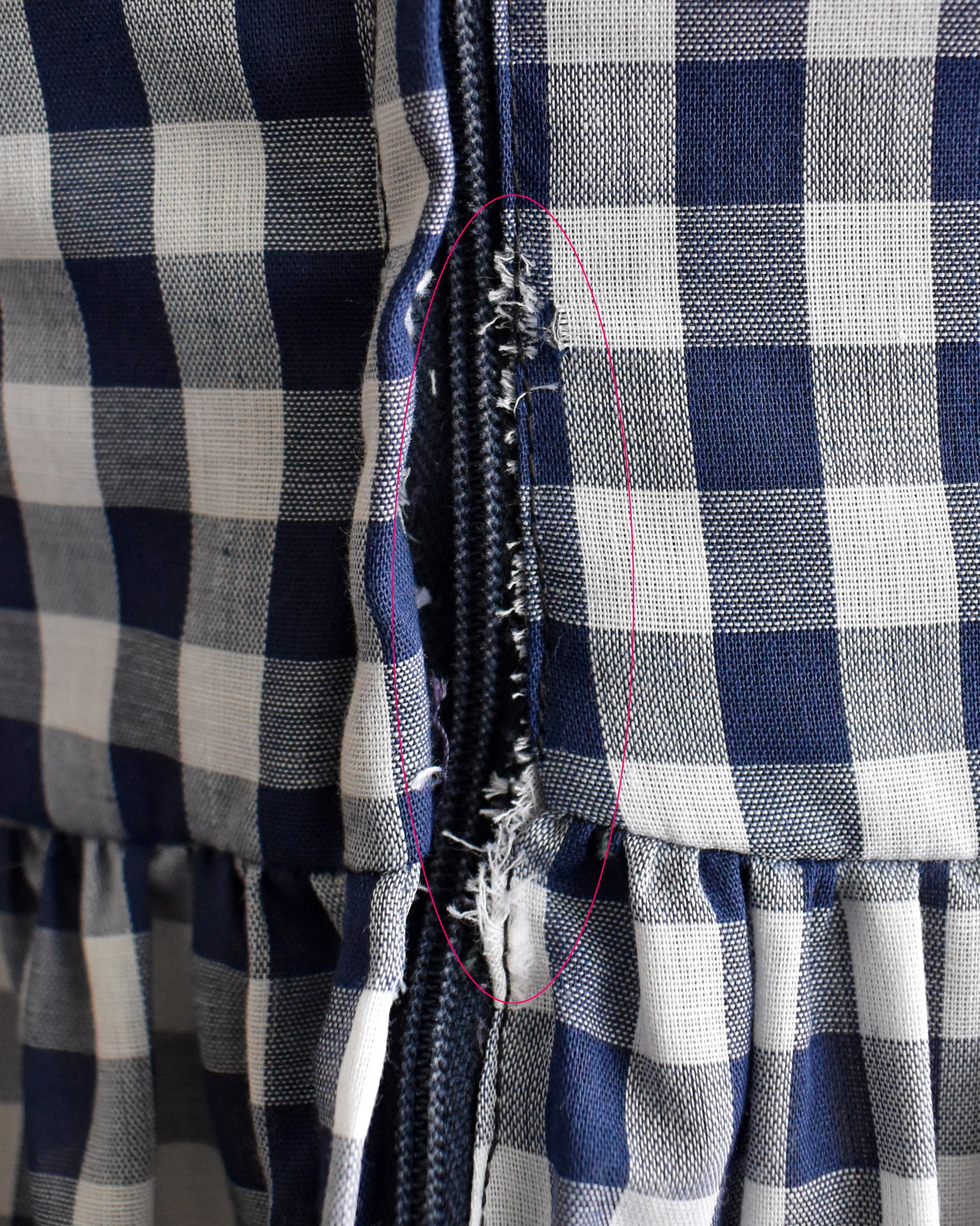 Close-up of a navy and white gingham fabric garment with a frayed seam near the center, highlighted by a pink stitched outline.
