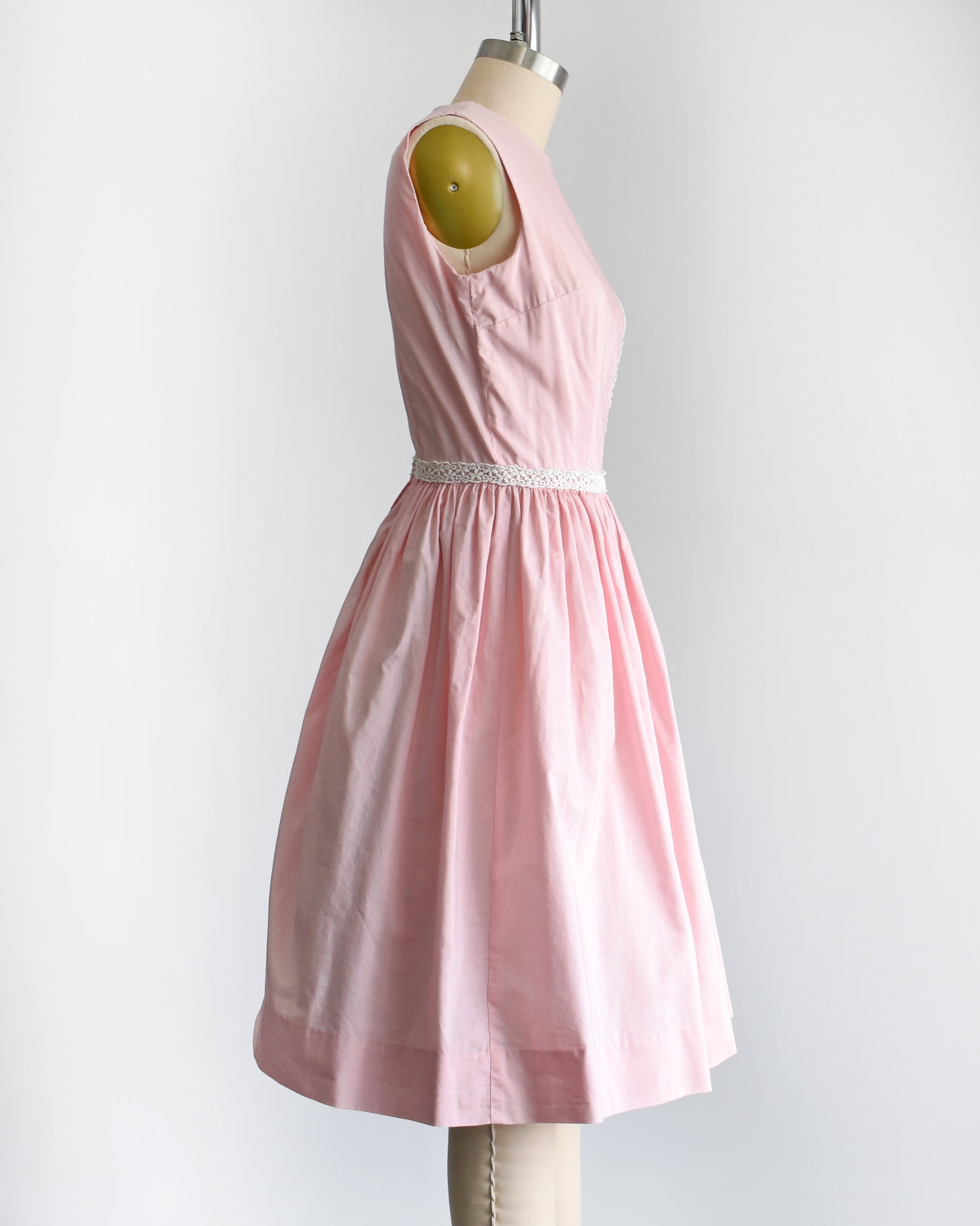 side view of a late 1950s early 1960s pink dress with white floral lace trim around the waist