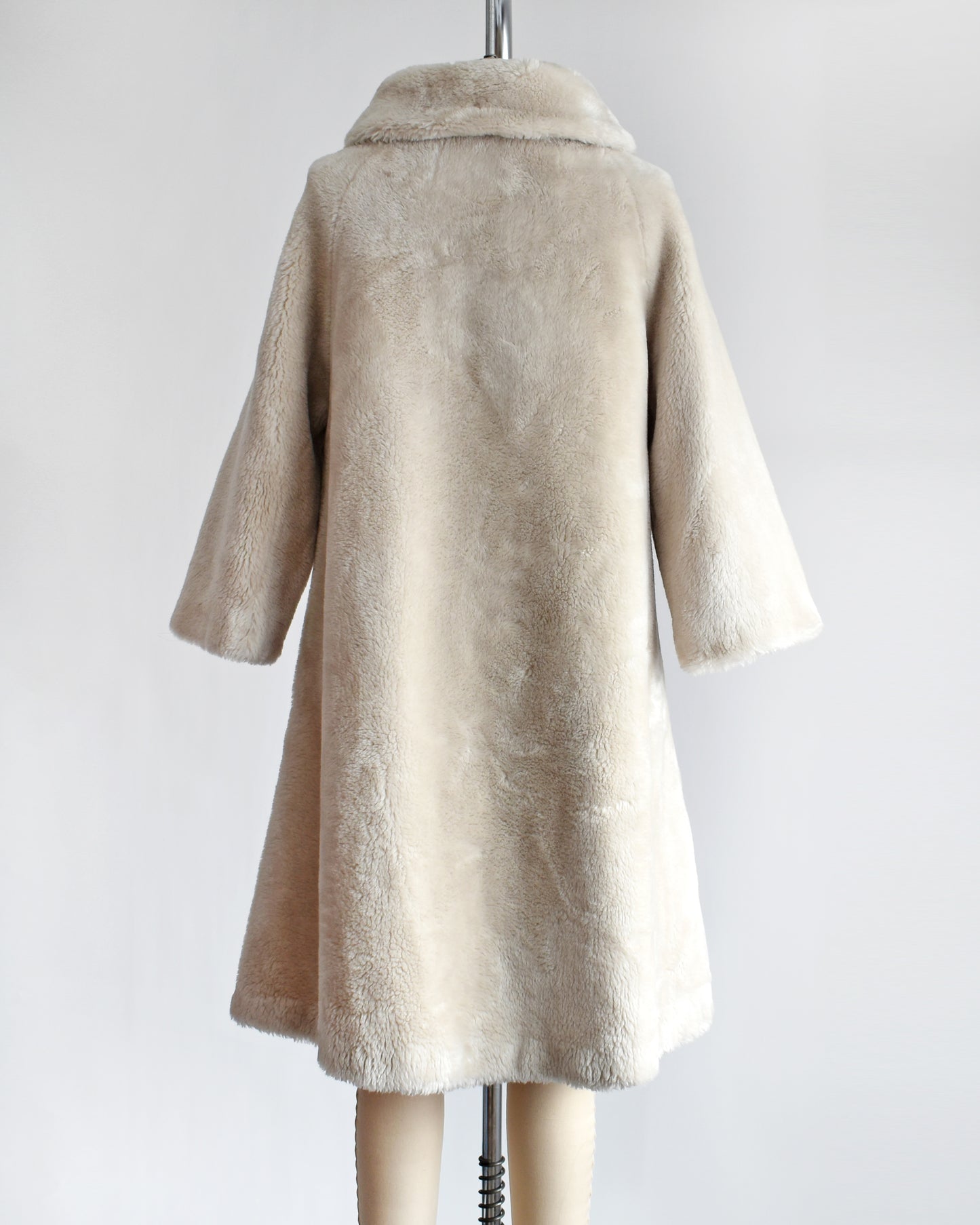 Back view of a vintage 1960s plush cream faux fur coat that features a Peter Pan style collar and three large buttons down the front