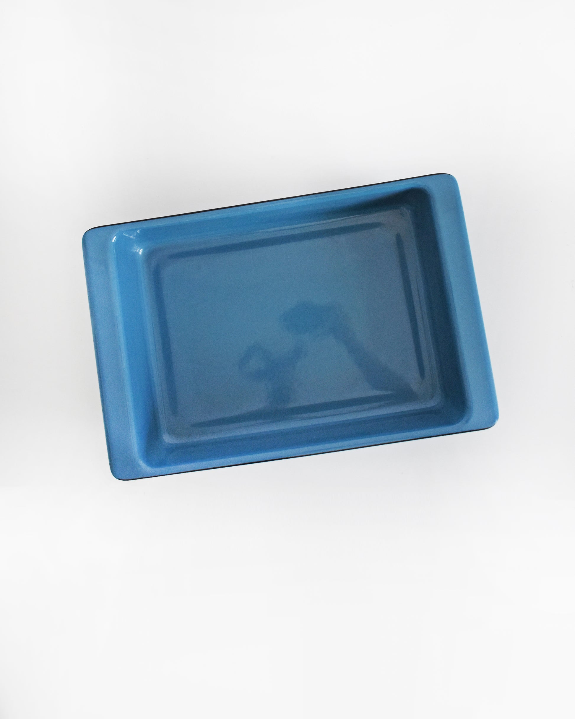 overhead shot of a mid century modern blue Cathrineholm lasagna pan that is rectangular with a decorative pattern of white lotus shapes on the sides, shown on a clean white background with a soft reflection.