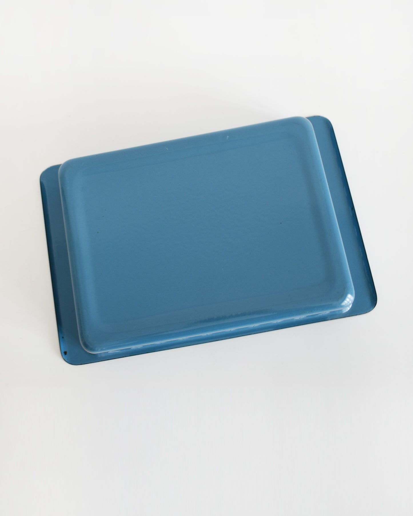 overhead shot of the underside of a mid century modern blue Cathrineholm lasagna pan that is rectangular with a decorative pattern of white lotus shapes on the sides, shown on a clean white background with a soft reflection.