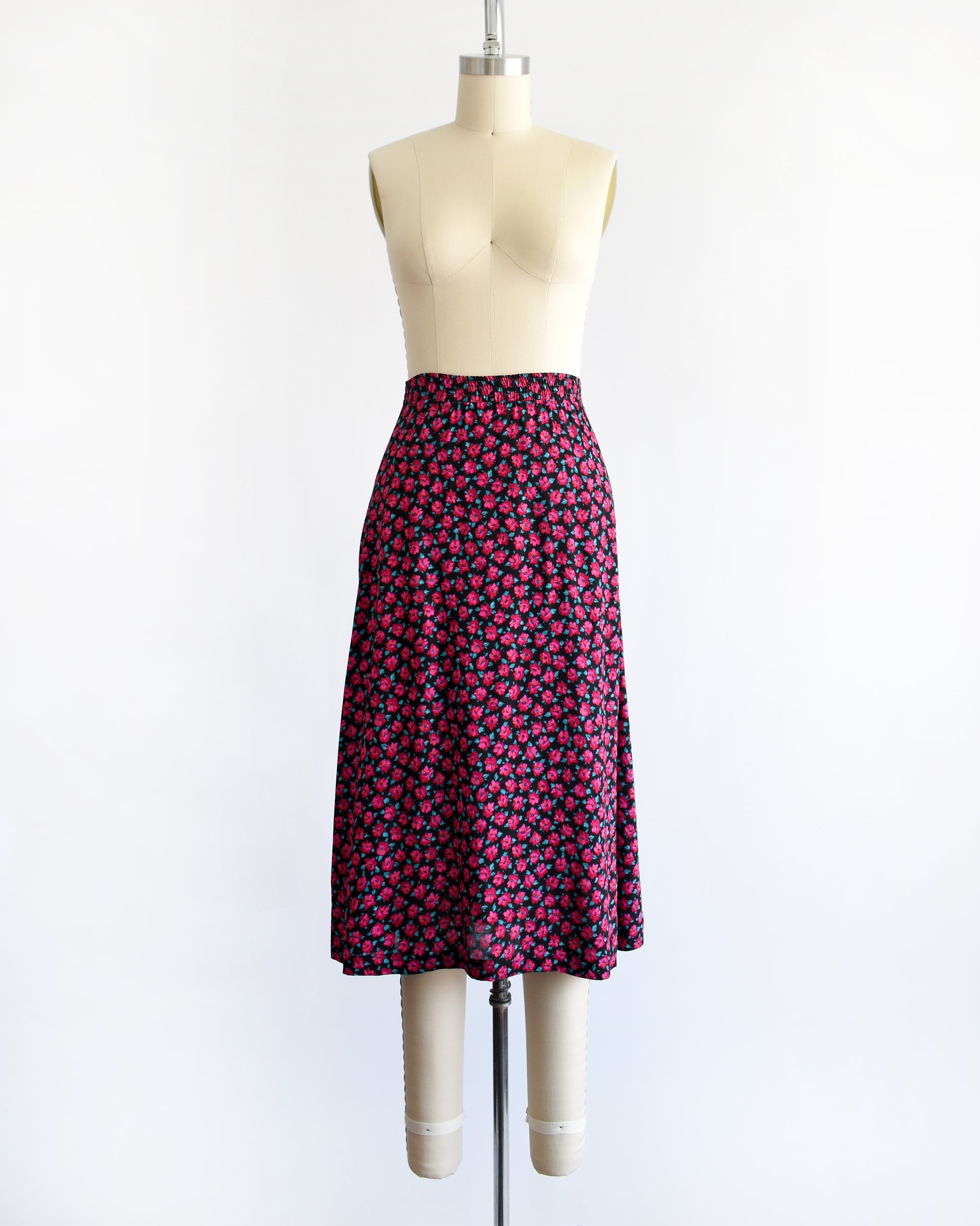 A vintage 1990s high-waisted A-line skirt with a dense pink and dark red floral print, displayed on a cream-colored dress form mannequin against a plain white background.