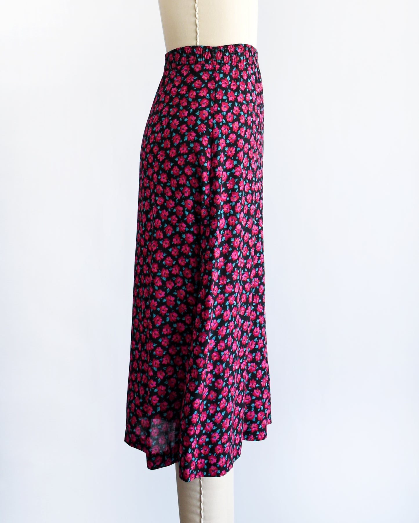 side view of a vintage 1990s high-waisted A-line skirt with a dense pink and dark red floral print, displayed on a cream-colored dress form mannequin against a plain white background.