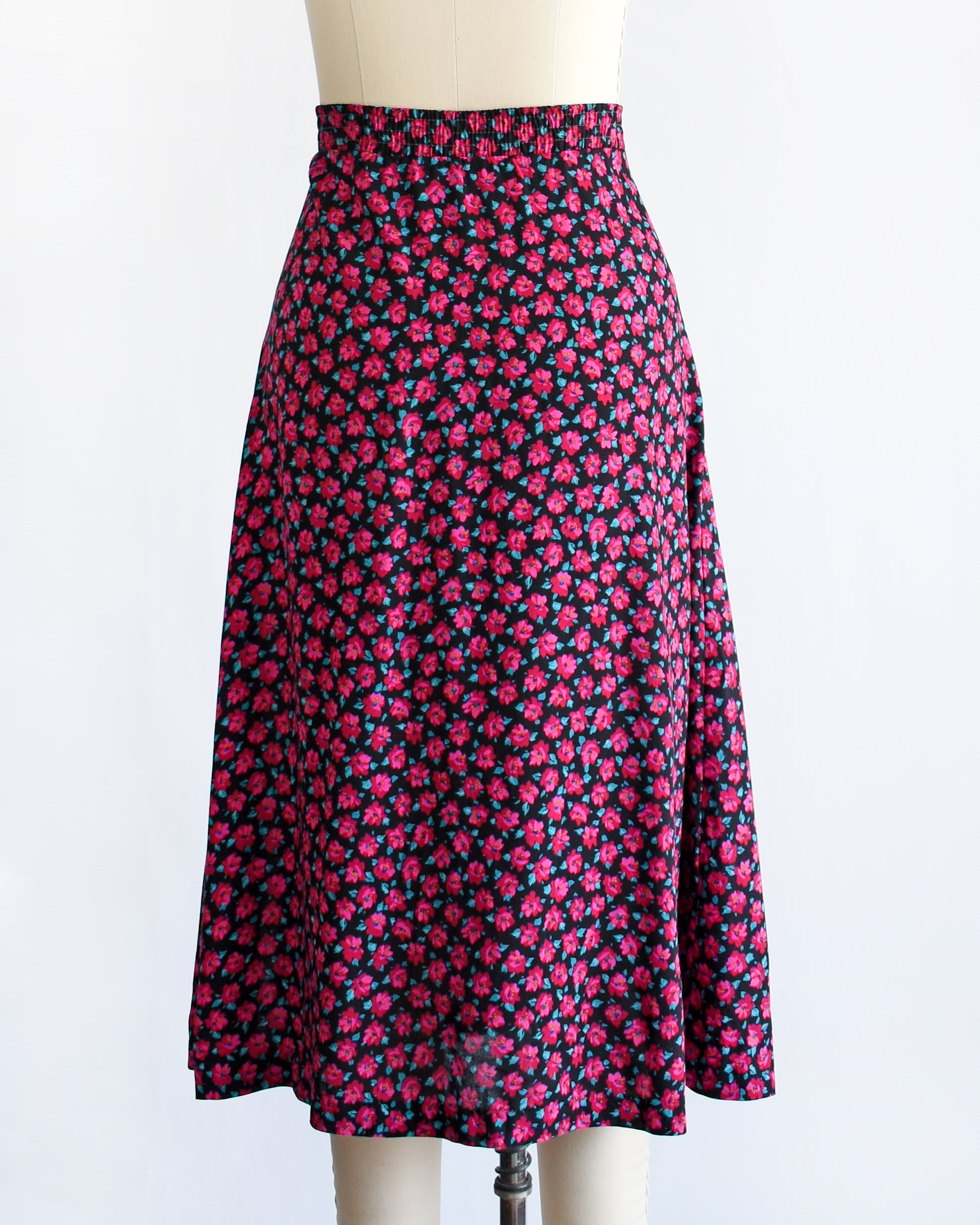 back view of a vintage 1990s high-waisted A-line skirt with a dense pink and dark red floral print, displayed on a cream-colored dress form mannequin against a plain white background.