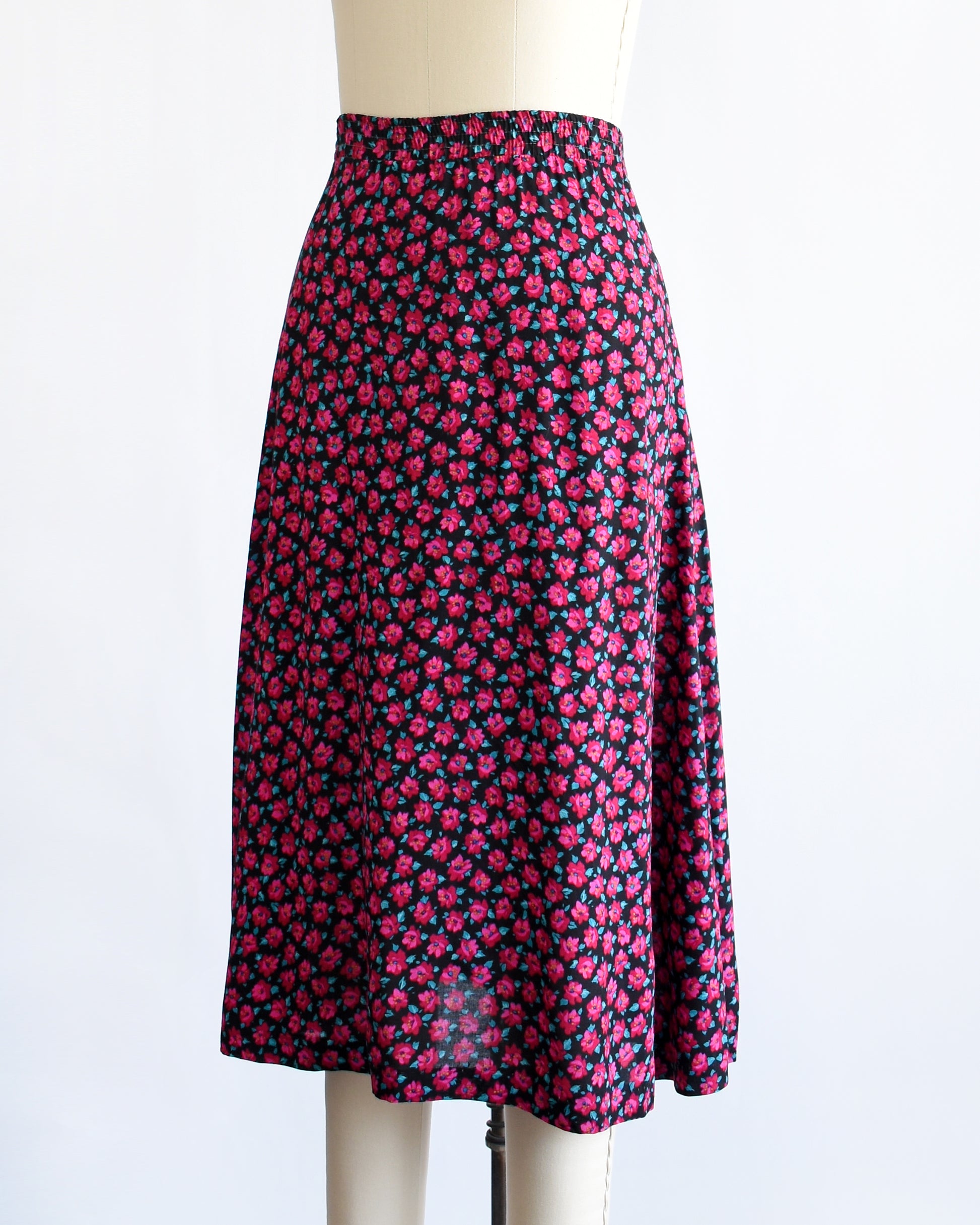 side front view of a vintage 1990s high-waisted A-line skirt with a dense pink and dark red floral print, displayed on a cream-colored dress form mannequin against a plain white background.