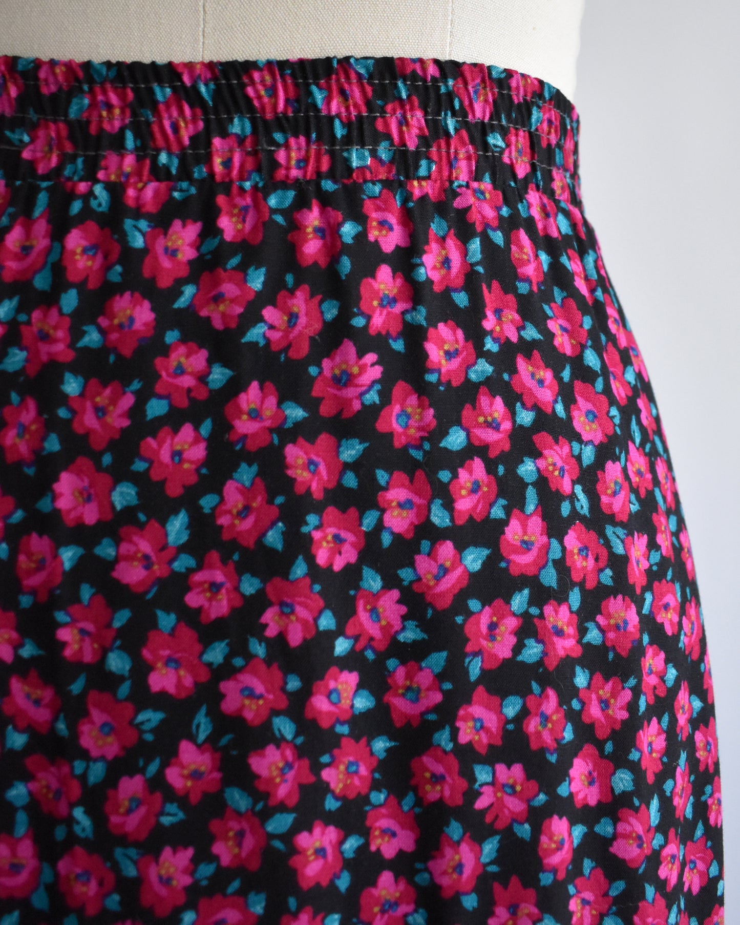 A close-up of a skirt or dress fabric on a mannequin, featuring a black background with a dense pink and blue floral print.