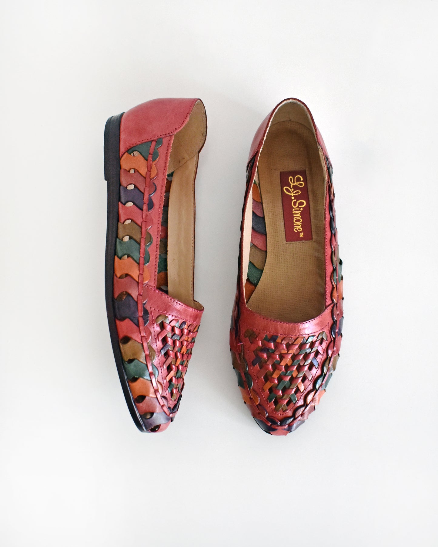 A pair of vintage 1980s women's pointed-toe flat shoes featuring a woven leather upper in shades of red, orange, and green with a dark brown sole, shown on a plain white background.