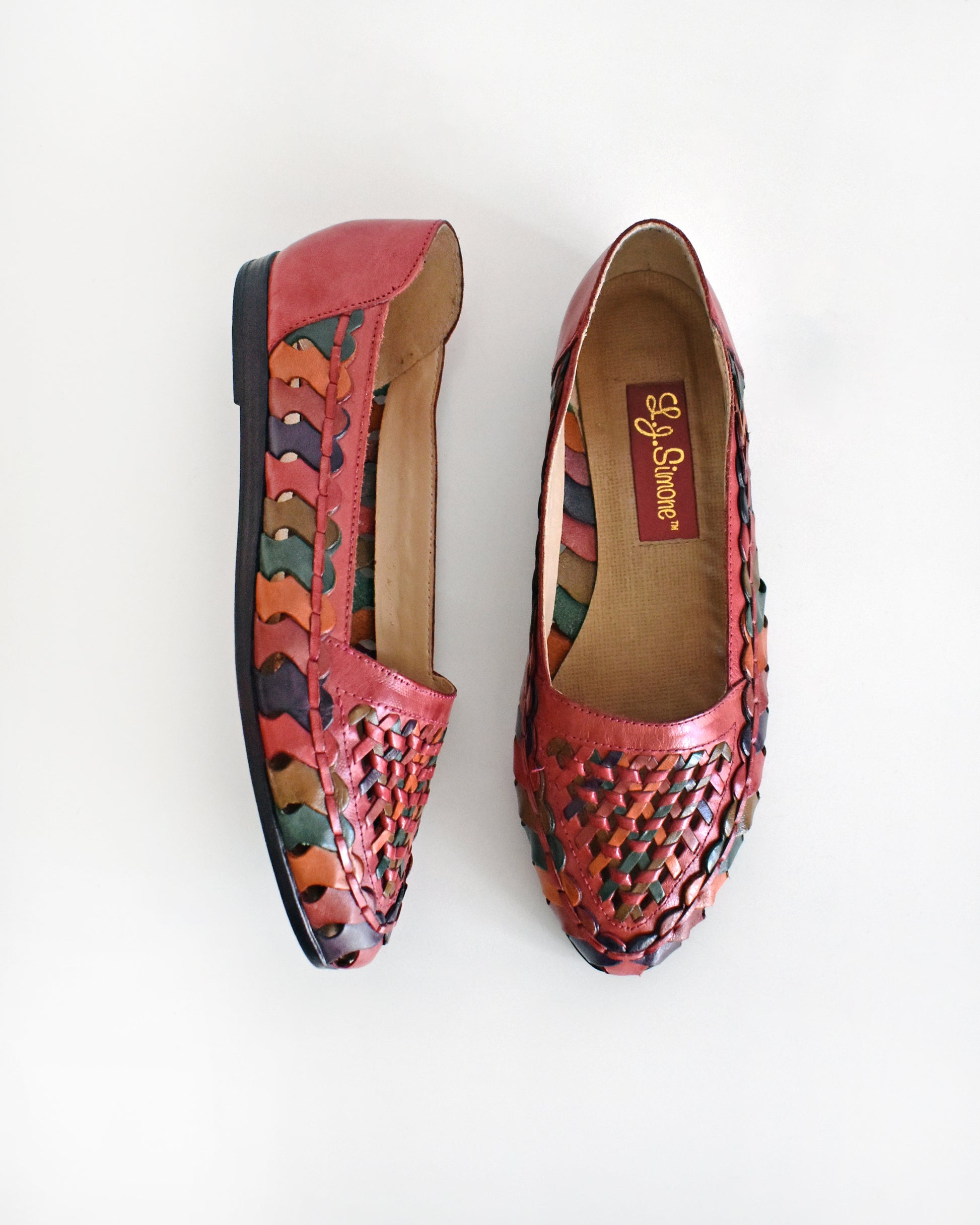 A pair of vintage 1980s women's pointed-toe flat shoes featuring a woven leather upper in shades of red, orange, and green with a dark brown sole, shown on a plain white background.