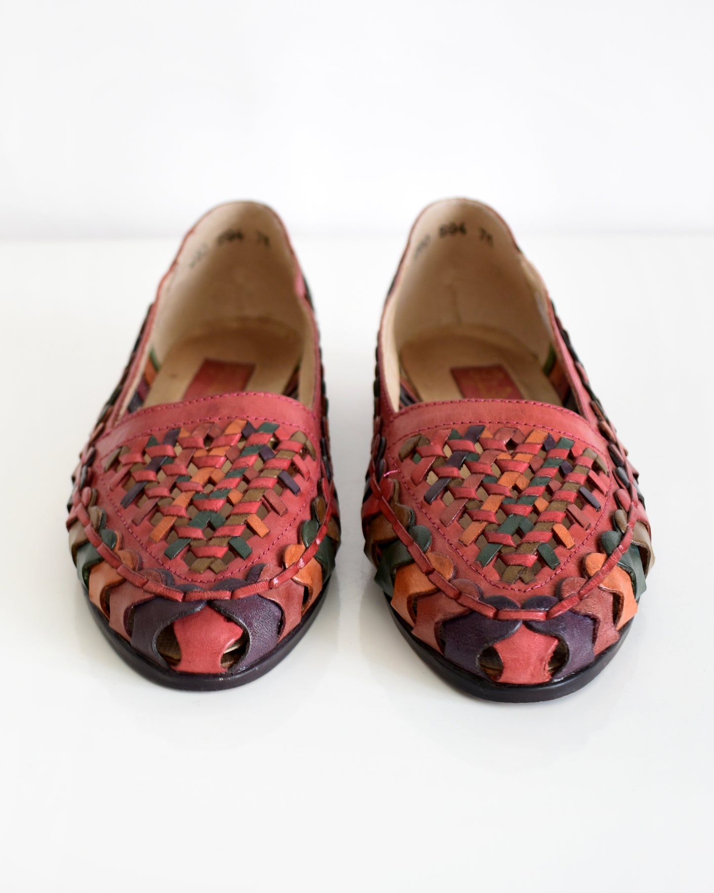 A pair of vintage 1980s women's pointed-toe flat shoes featuring a woven leather upper in shades of red, orange, and green with a dark brown sole, shown on a plain white background.