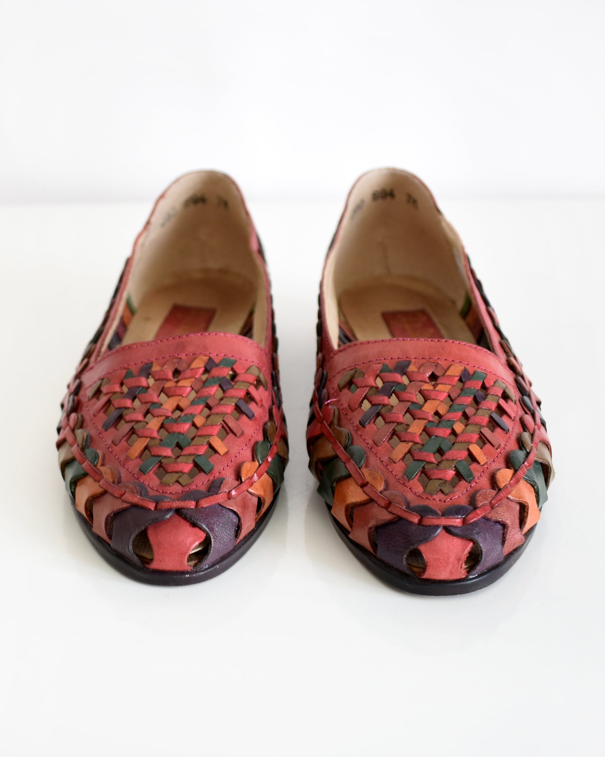 A pair of vintage 1980s women's pointed-toe flat shoes featuring a woven leather upper in shades of red, orange, and green with a dark brown sole, shown on a plain white background.