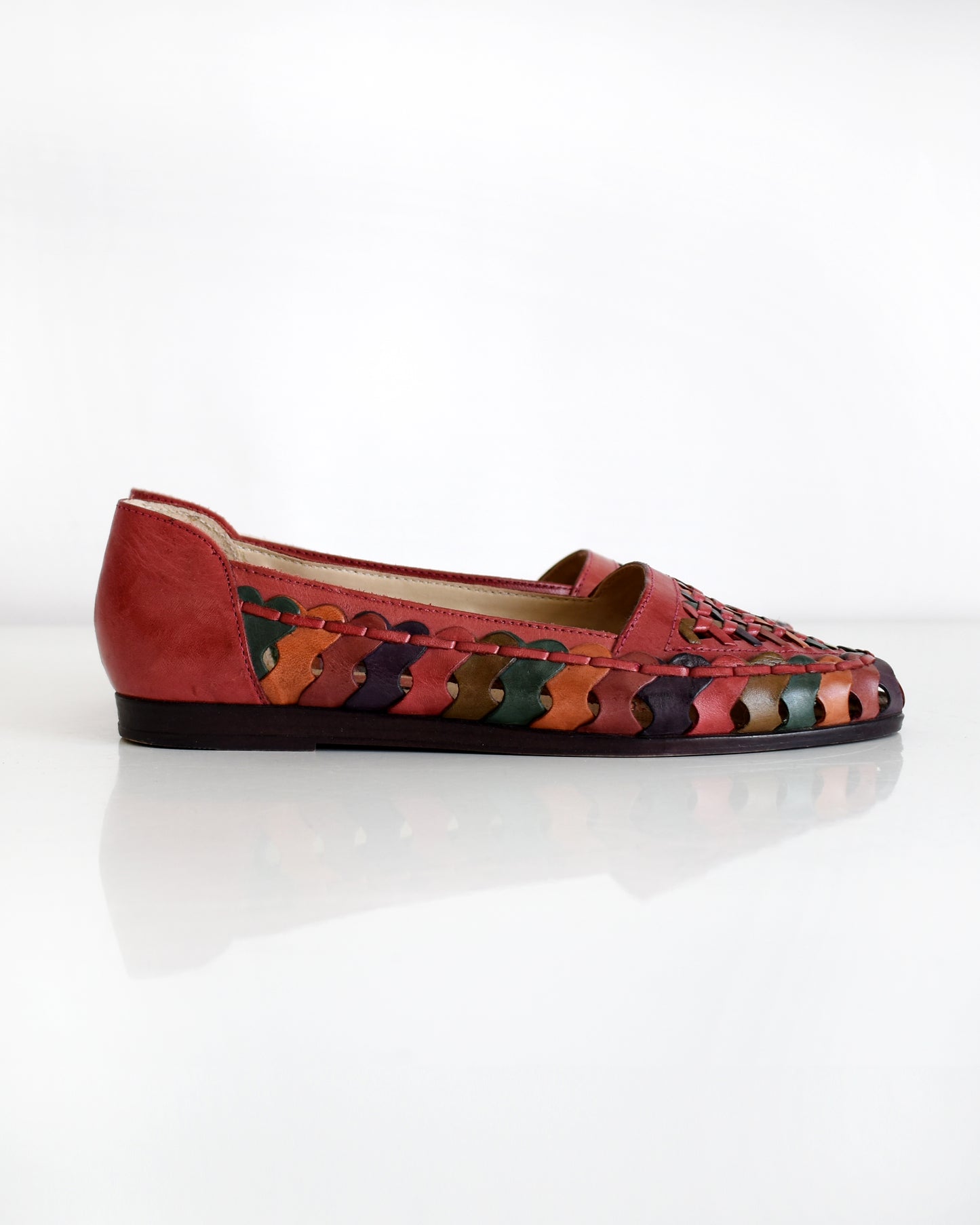 A pair of vintage 1980s women's pointed-toe flat shoes featuring a woven leather upper in shades of red, orange, and green with a dark brown sole, shown on a plain white background.