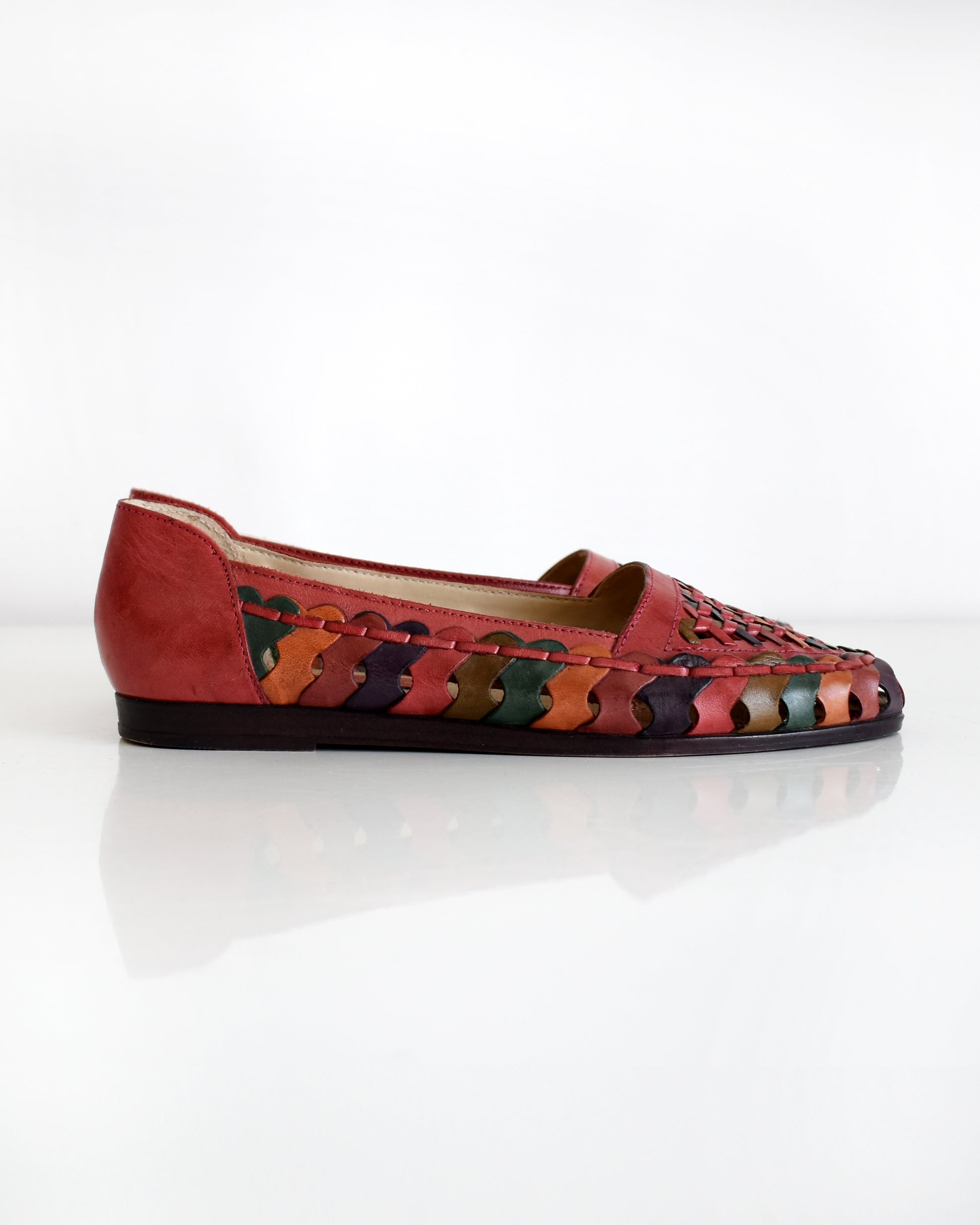 A pair of vintage 1980s women's pointed-toe flat shoes featuring a woven leather upper in shades of red, orange, and green with a dark brown sole, shown on a plain white background.
