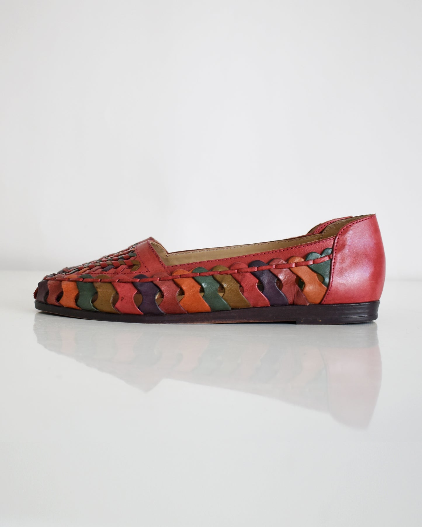 A pair of vintage 1980s women's pointed-toe flat shoes featuring a woven leather upper in shades of red, orange, and green with a dark brown sole, shown on a plain white background.