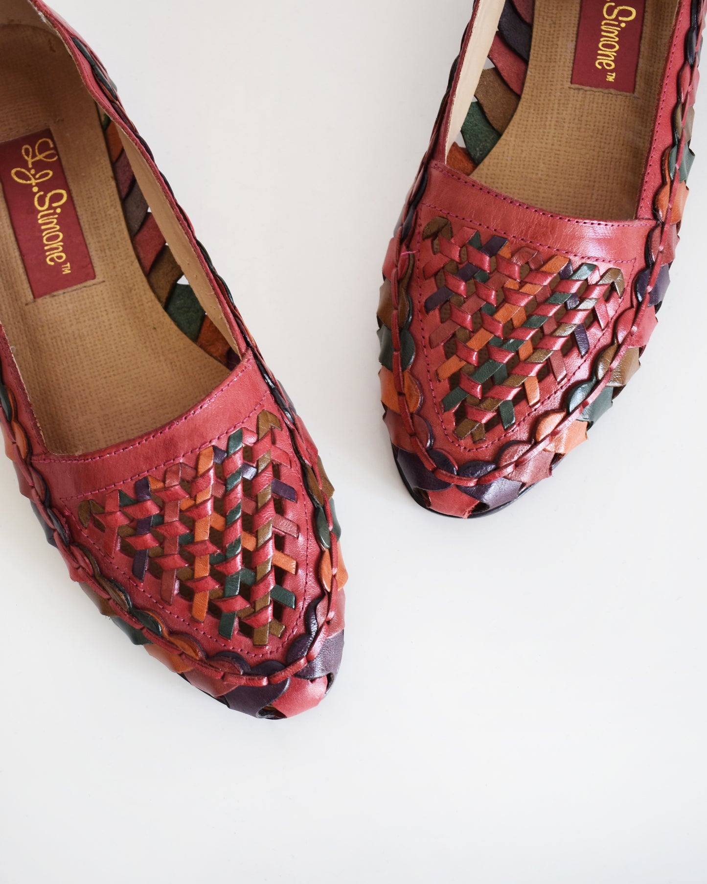 A pair of vintage 1980s women's pointed-toe flat shoes featuring a woven leather upper in shades of red, orange, and green with a dark brown sole, shown on a plain white background.