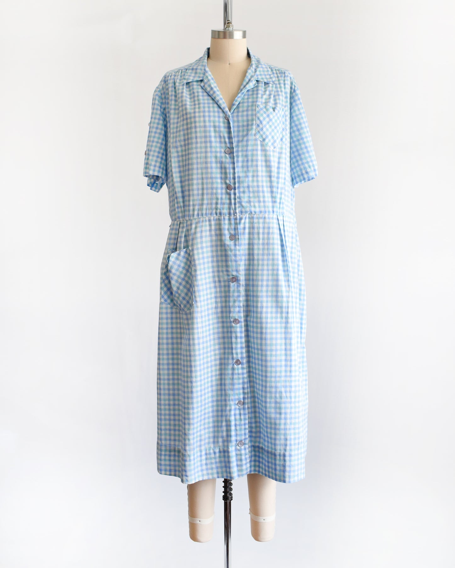 A vintage 1950s light blue and white gingham short-sleeve button-front dress displayed on a mannequin against a plain white background.