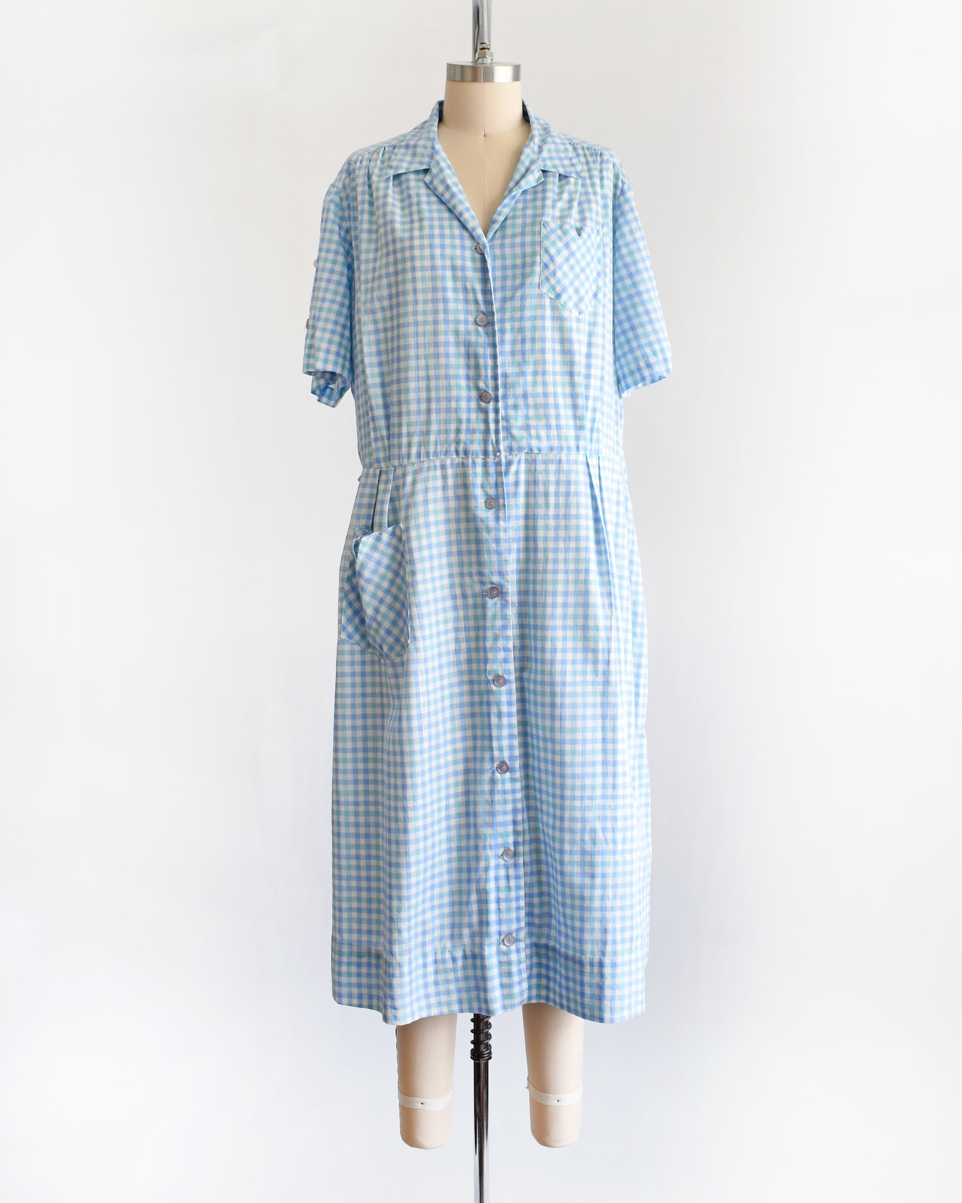 A vintage 1950s light blue and white gingham short-sleeve button-front dress displayed on a mannequin against a plain white background.