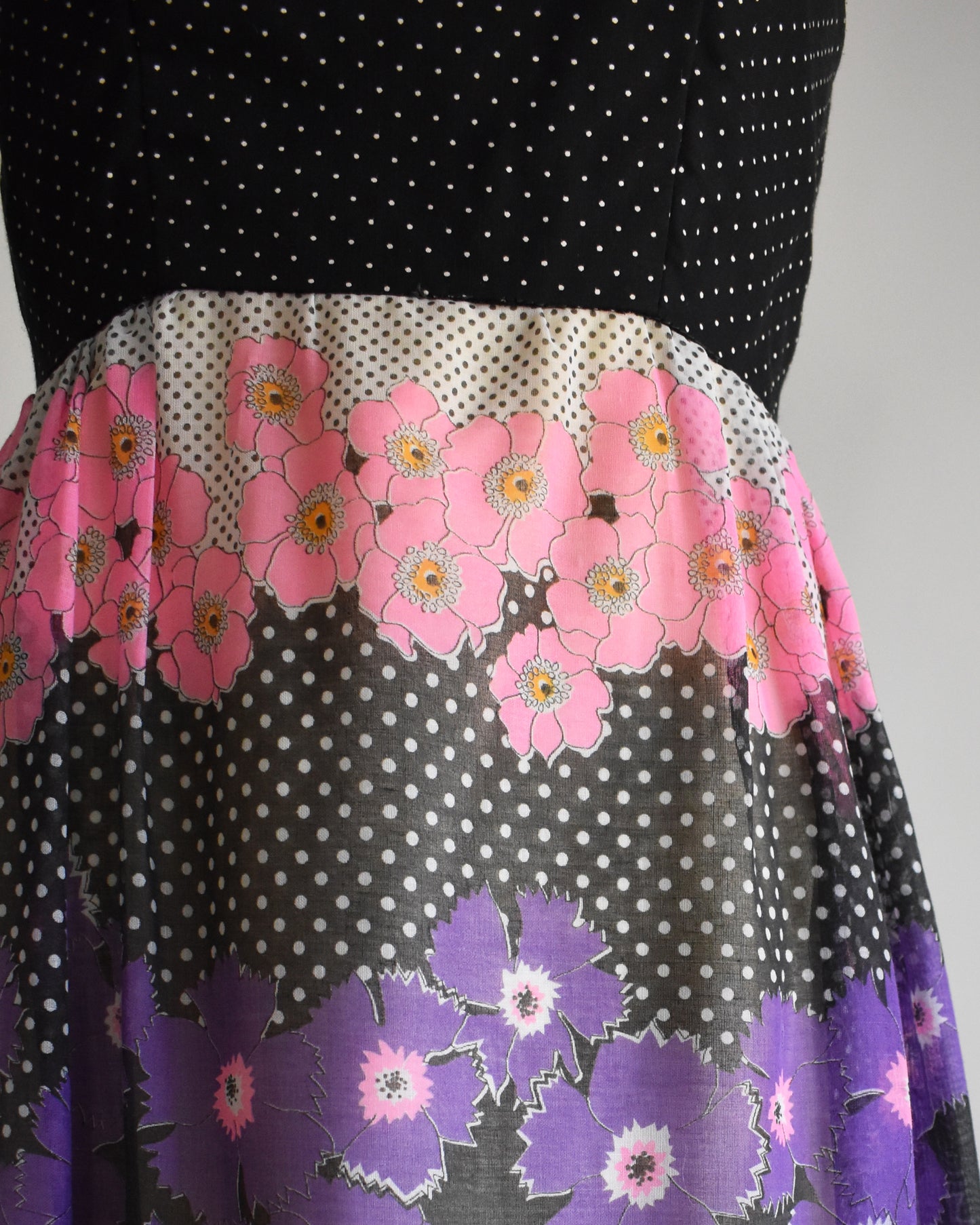 close up of the waist of a vintage 1970s black floral dress  on a mannequin against a white background