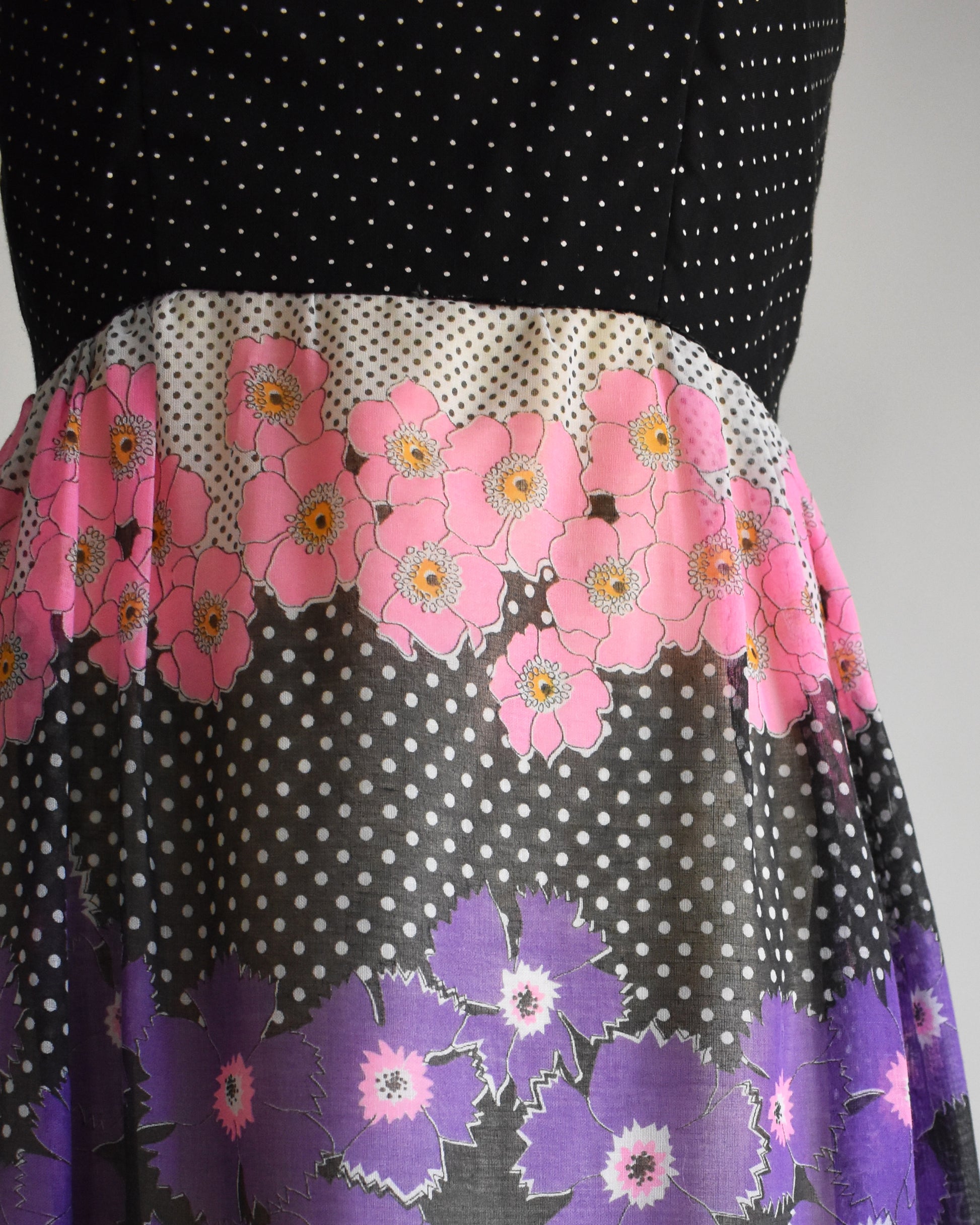 close up of the waist of a vintage 1970s black floral dress  on a mannequin against a white background
