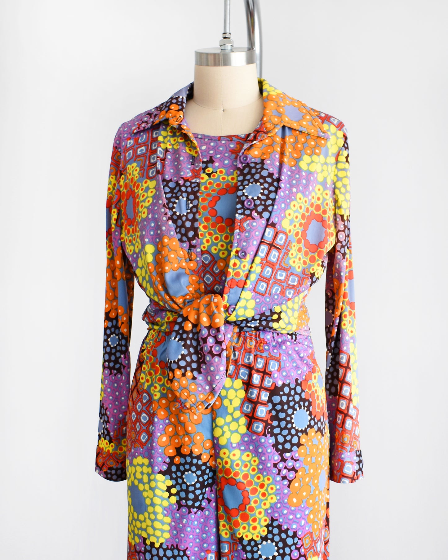 Side front view of a vibrant vintage 1970 mod floral pantsuit three piece set. The blouse is tied at the waist