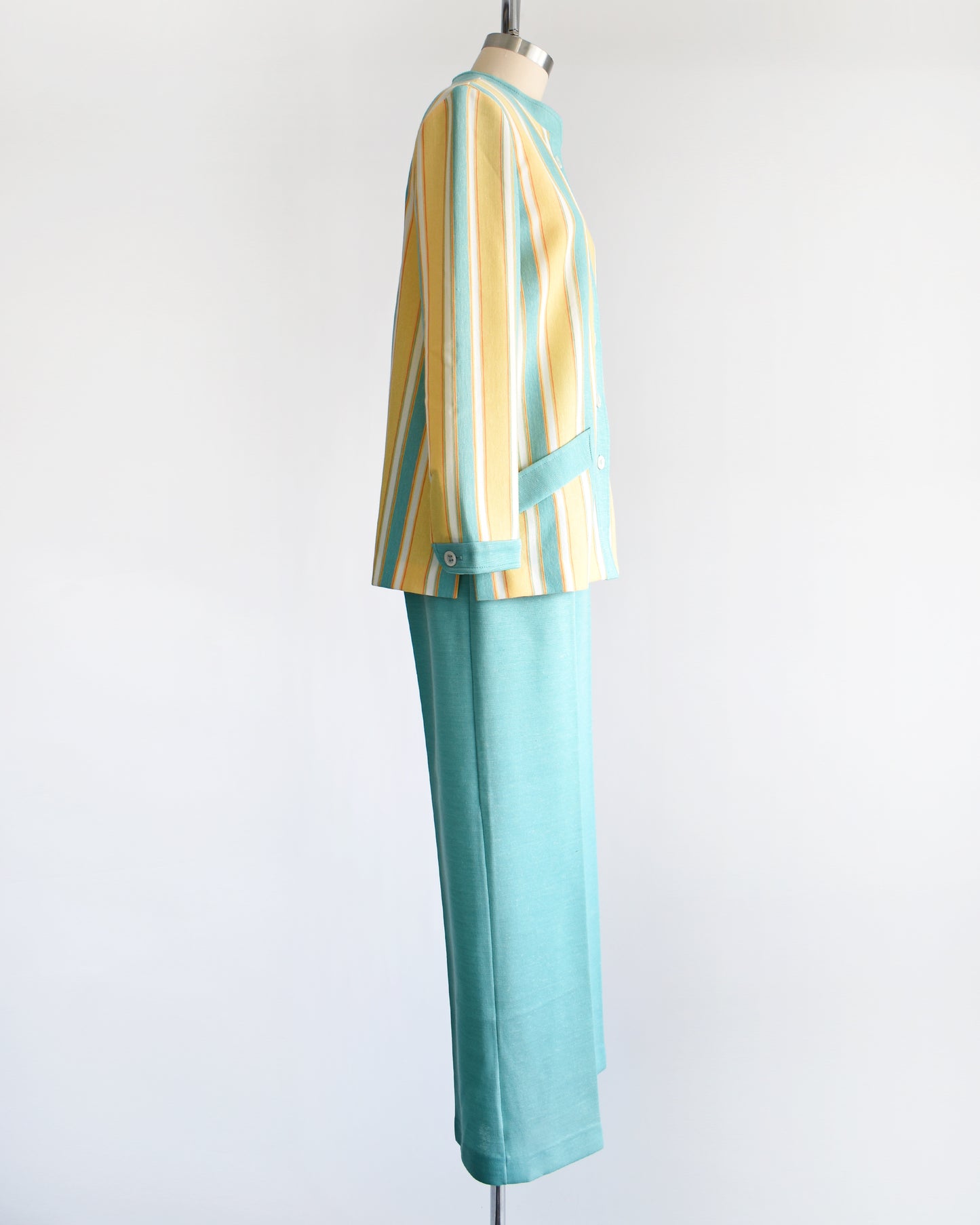 side view of a vintage 1970s two piece pantsuit. The top is yellow, blue, white and orange striped, and the pants are the same matching blue.